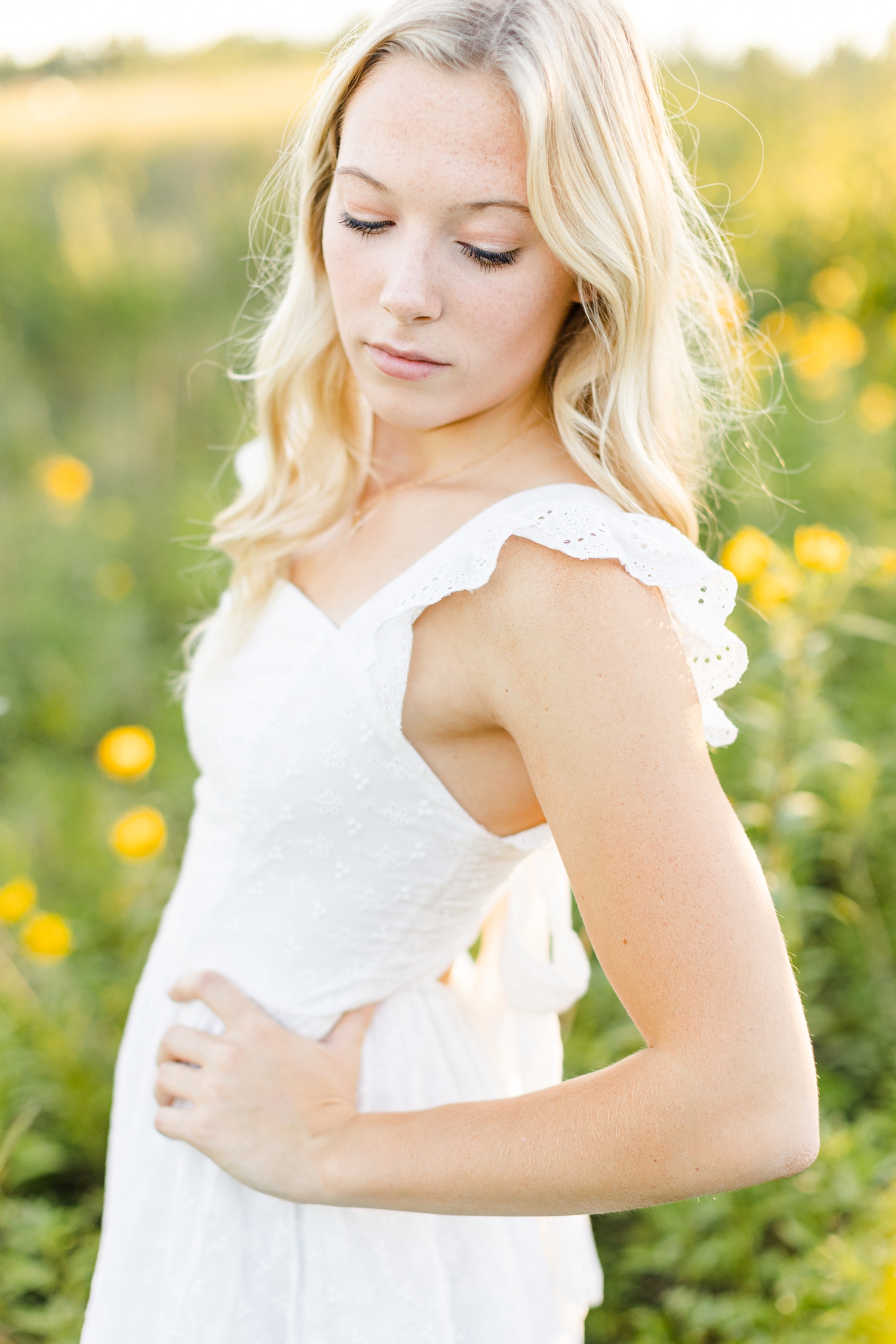 Shelby looks down and over her shoulder in a field of yellow wildflowers at Water's Edge Nature Center | CB Studio