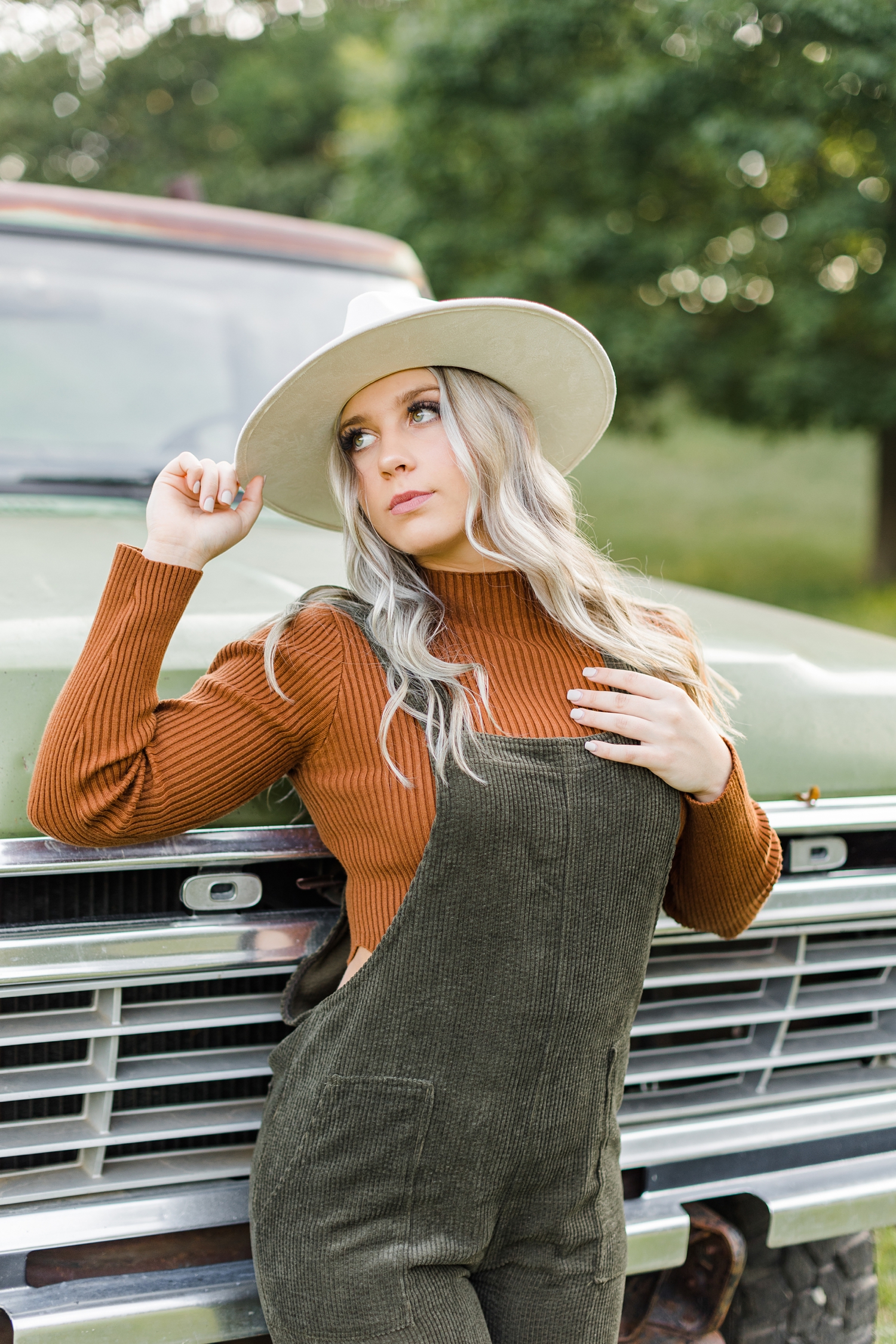 Shelby leans against the front end of a green 72 Ford truck in the middle of a grassy pasture | CB Studio