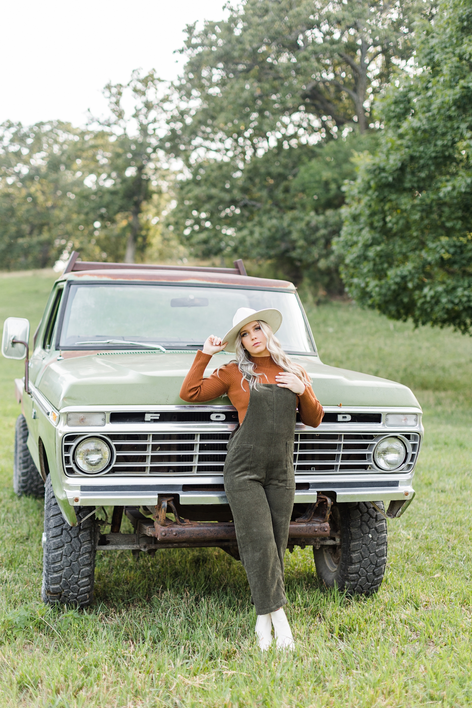 Shelby leans against the front end of a green 72 Ford truck in the middle of a grassy pasture | CB Studio