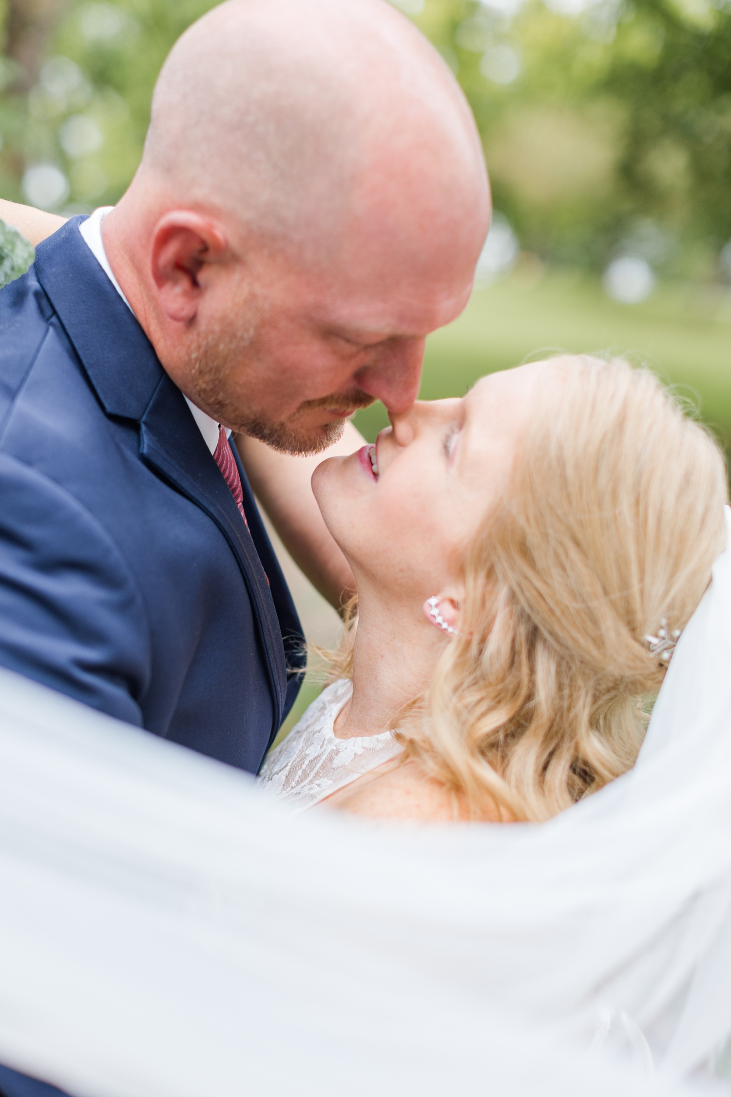James and Megan slowly kiss surrounded by Megan's wedding veil in Kennedy Park Fort Dodge, IA | CB Studio