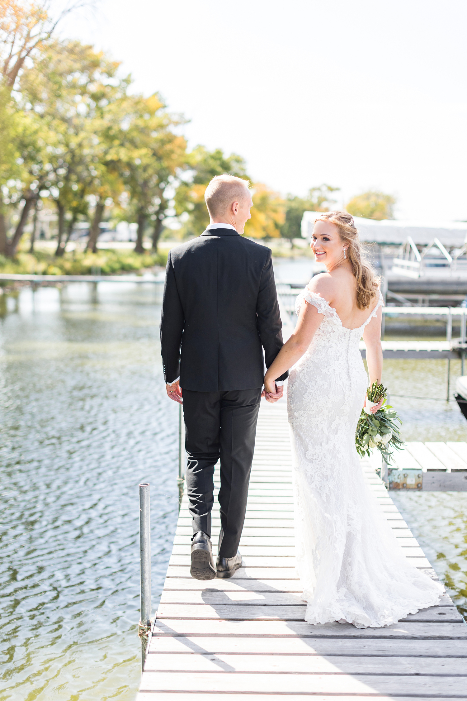 Brenna looks back as her groom, Jacob, leads her across a dock at Five Island Lake, Emmetsburg, Iowa | CB Studio