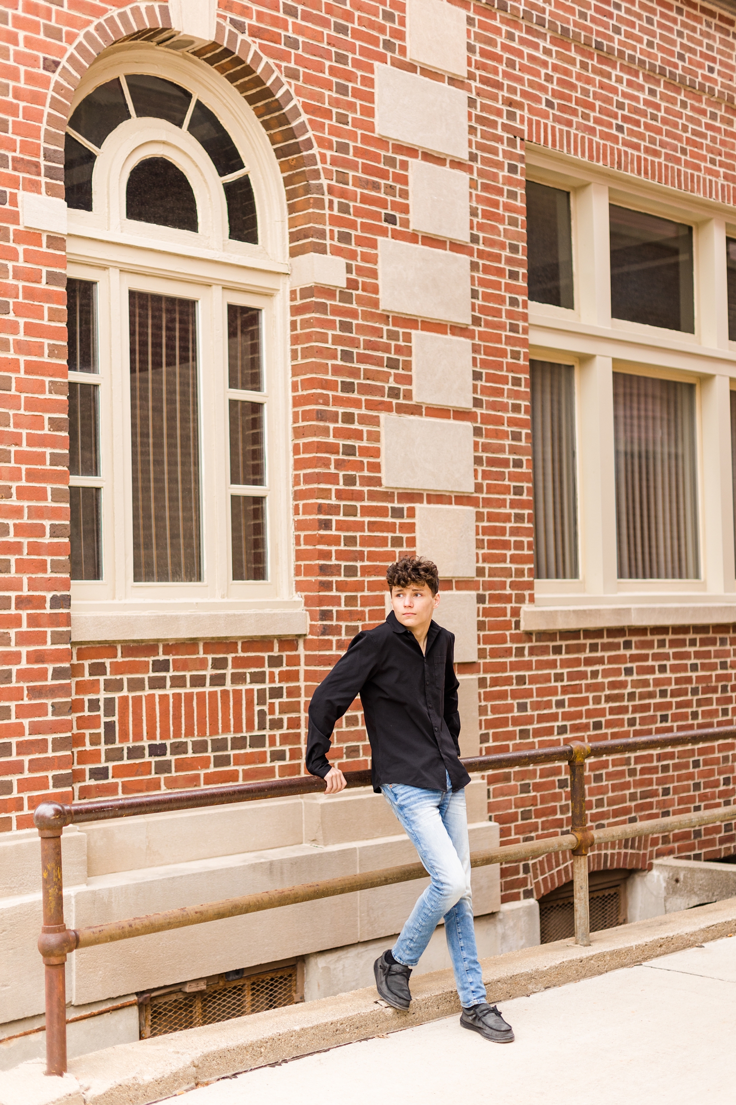 Joey leans against a stair railing along a historic building and looks off into the distance in downtown Algona, Iowa | CB Studio