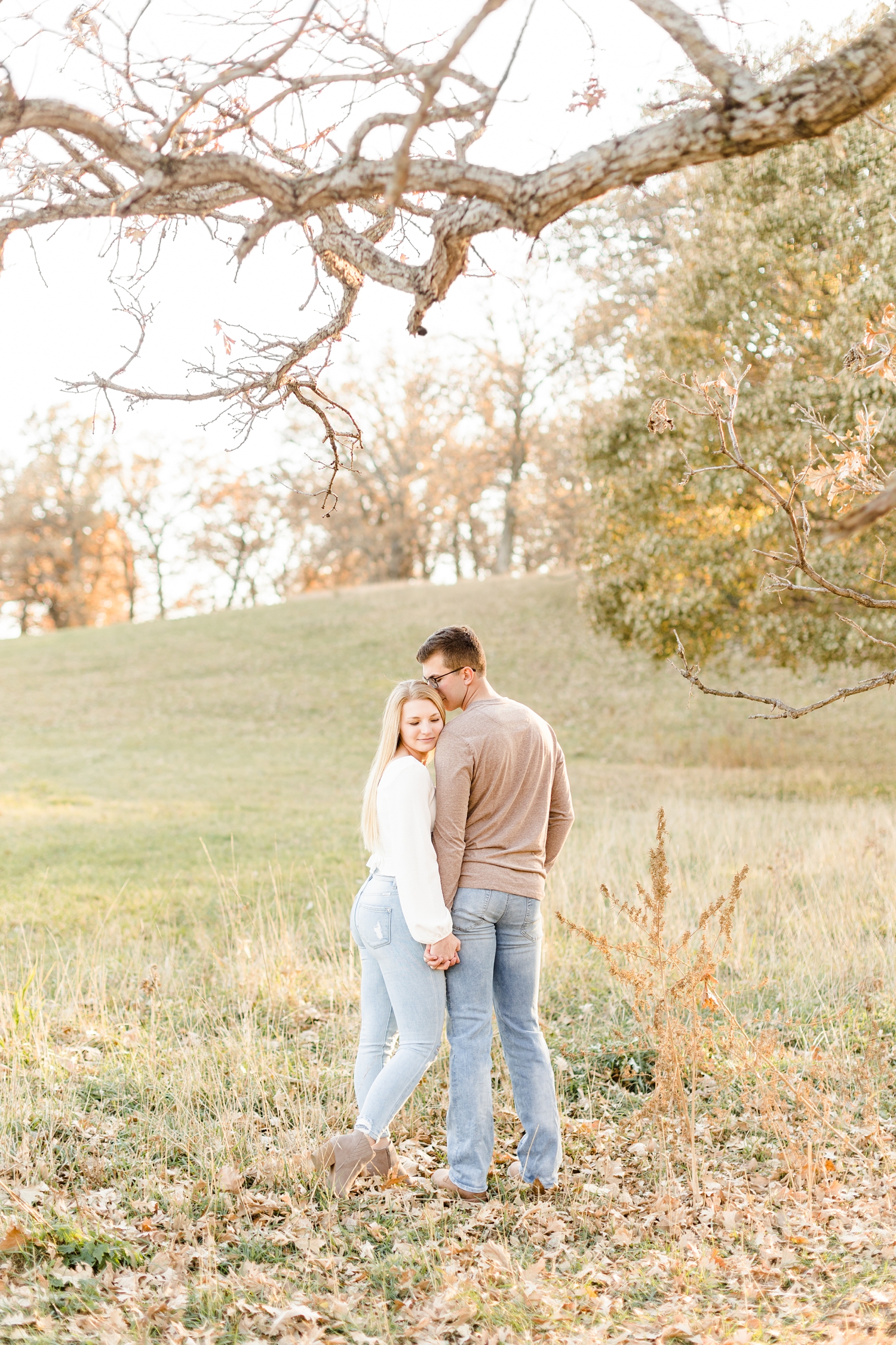 Quinton nuzzles Alli while standing and holding hands in a grassy pasture full of leaves | CB Studio