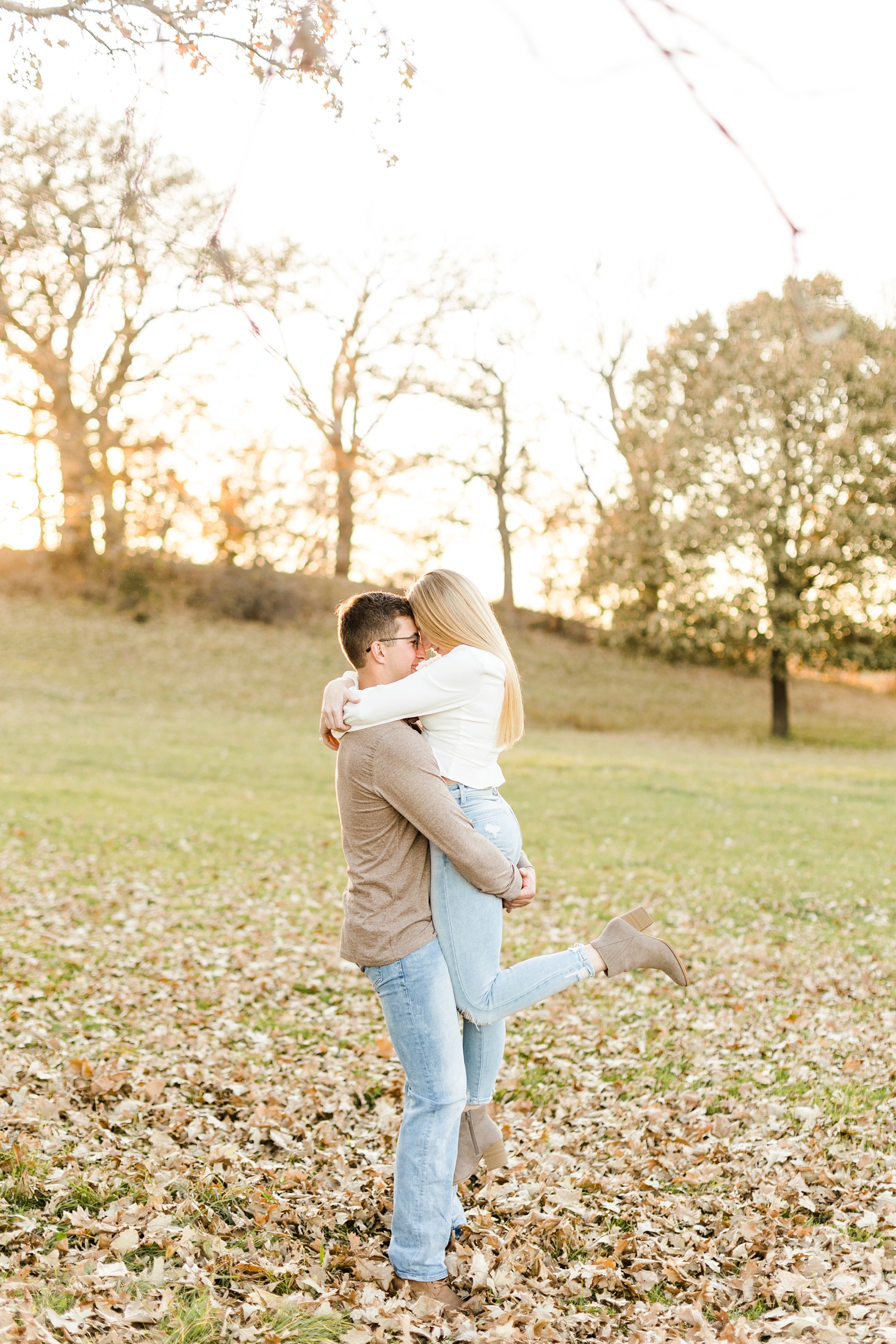 Quinton picks Alli up and rest foreheads together in a grassy pasture full of leaves during golden hour | CB Studio
