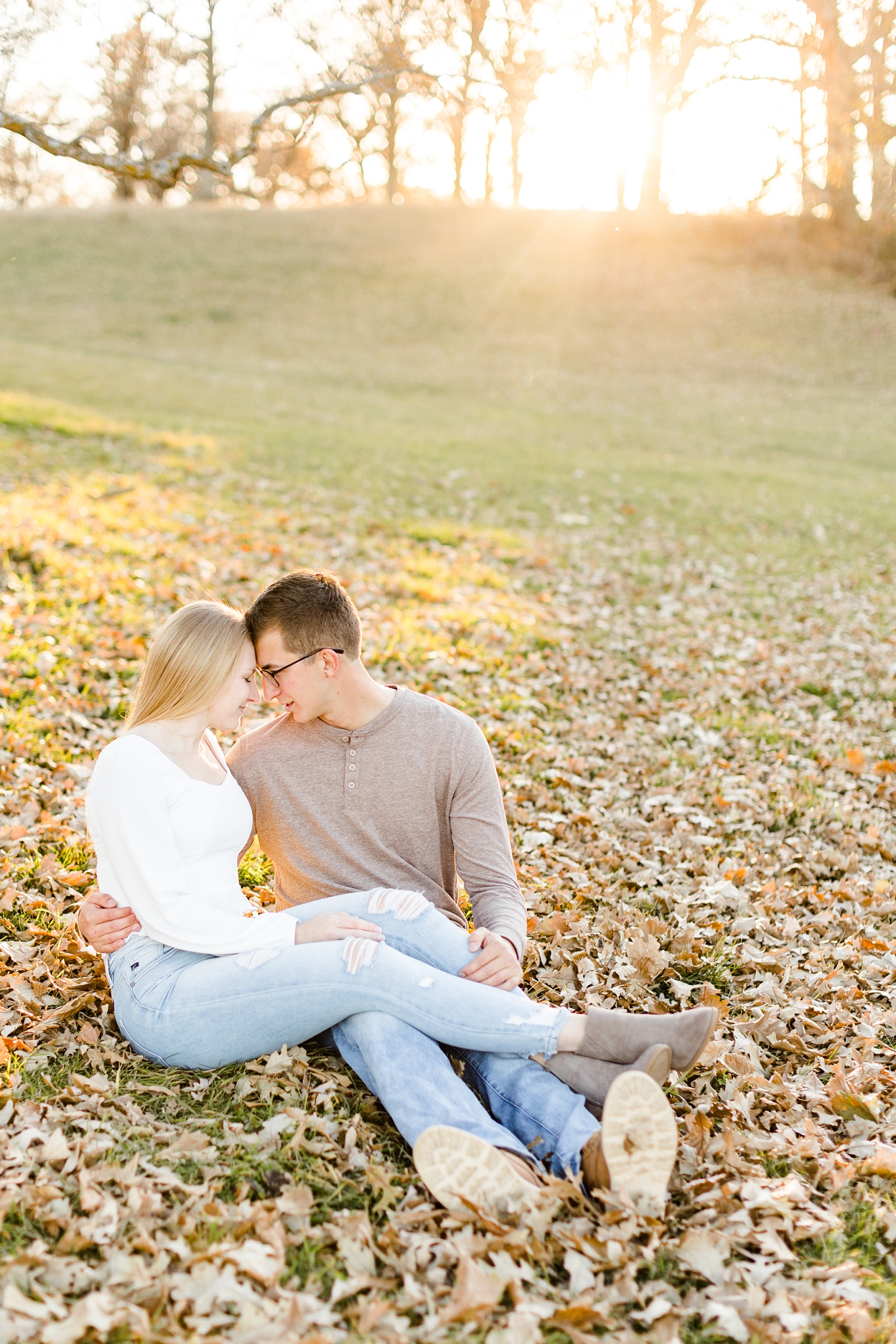 Alli and Quinton rest foreheads together while sitting in a grassy pasture full of leaves during sunset | CB Studio