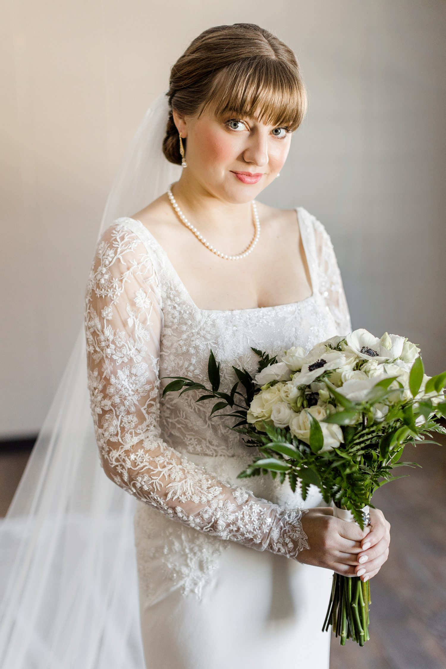 Bride, Madeline, dressed in a custom Stella York long sleeve wedding gown with custom cathedral length veil standing in a wooden church holding a white rose and anemone bouquet | CB Studio