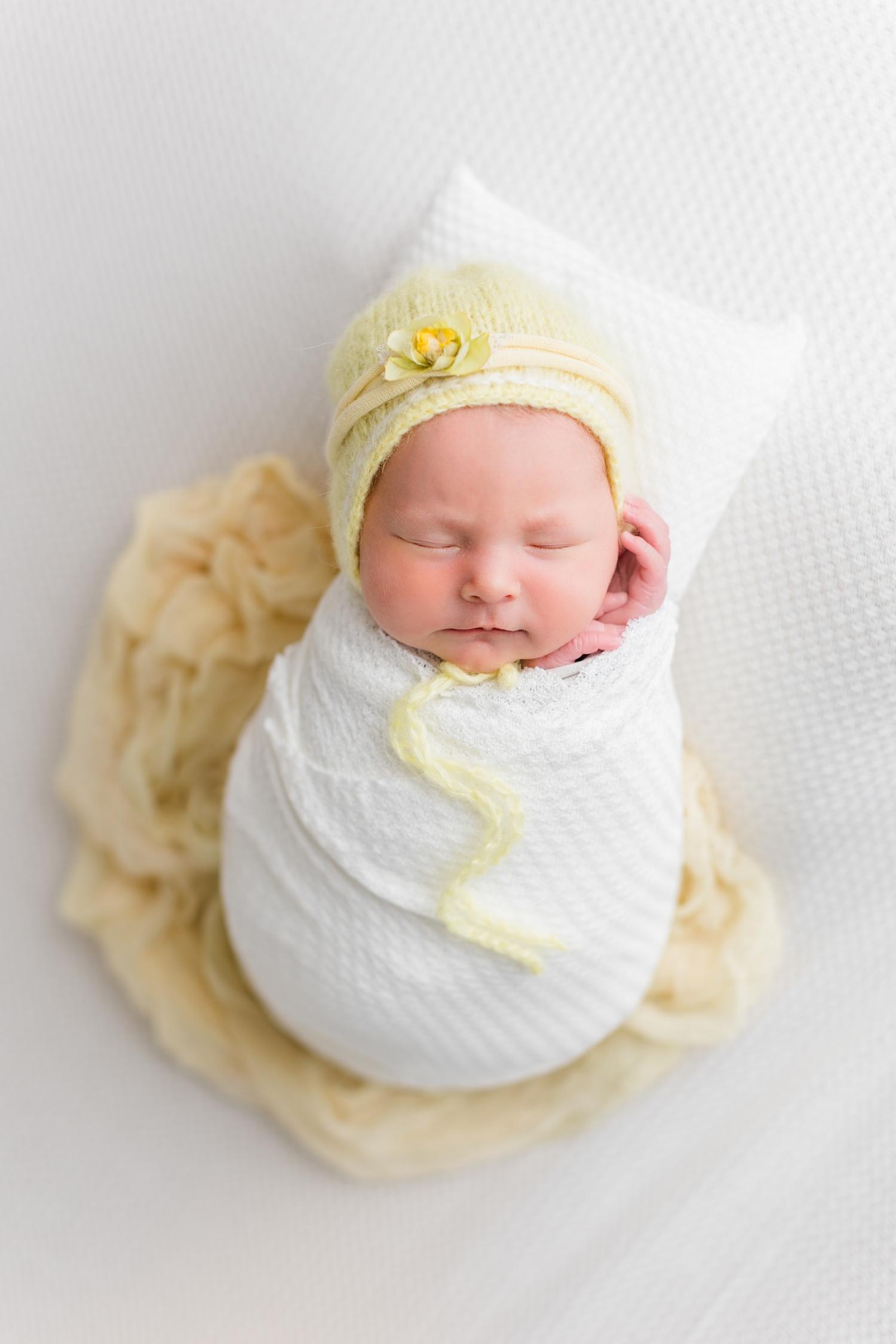 Baby Olivia wrapped in white laying on a soft yellow swaddle wearing a yellow bonnet with floral detail | CB Studio