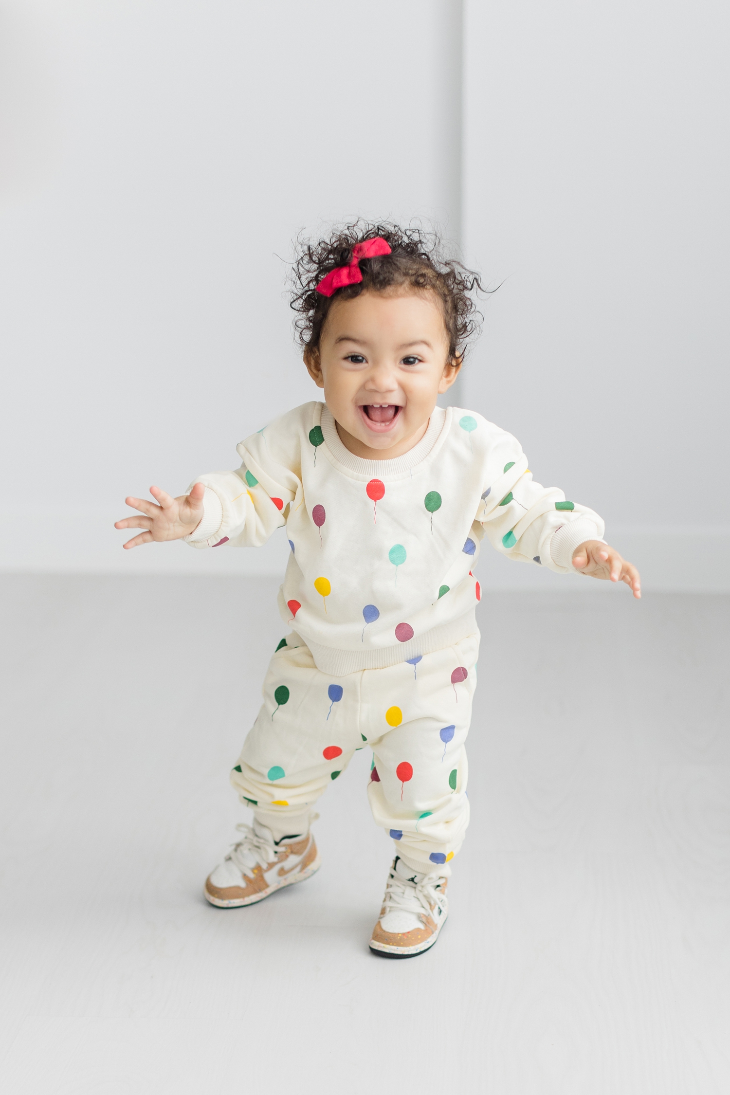 Baby Zoey full of smiles and excitement wearing a cream sweat set sprinkled with colorful balloons | CB Studio