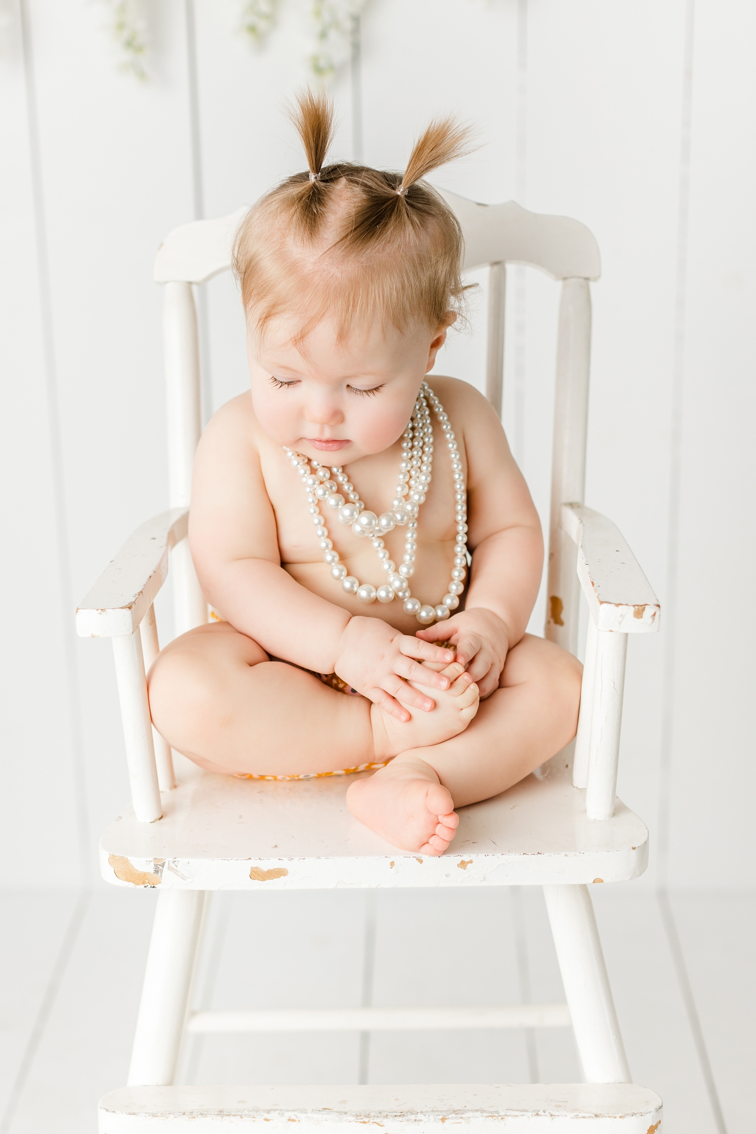 Baby Scarlett sits in a vintage high chair wearing antique pearls | CB Studio