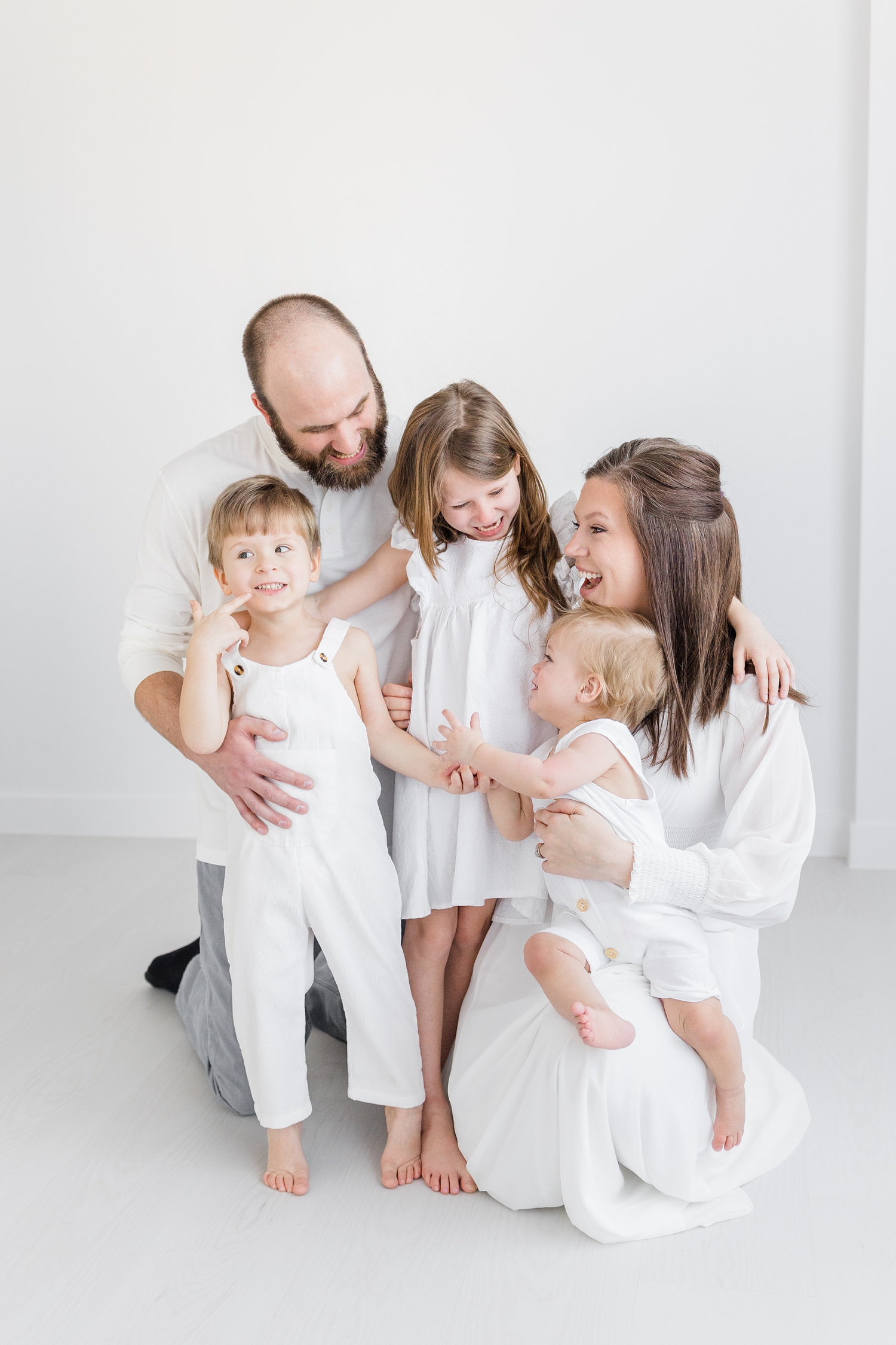 Schreiner family smile at each other during a signature white studio photography session | CB Studio