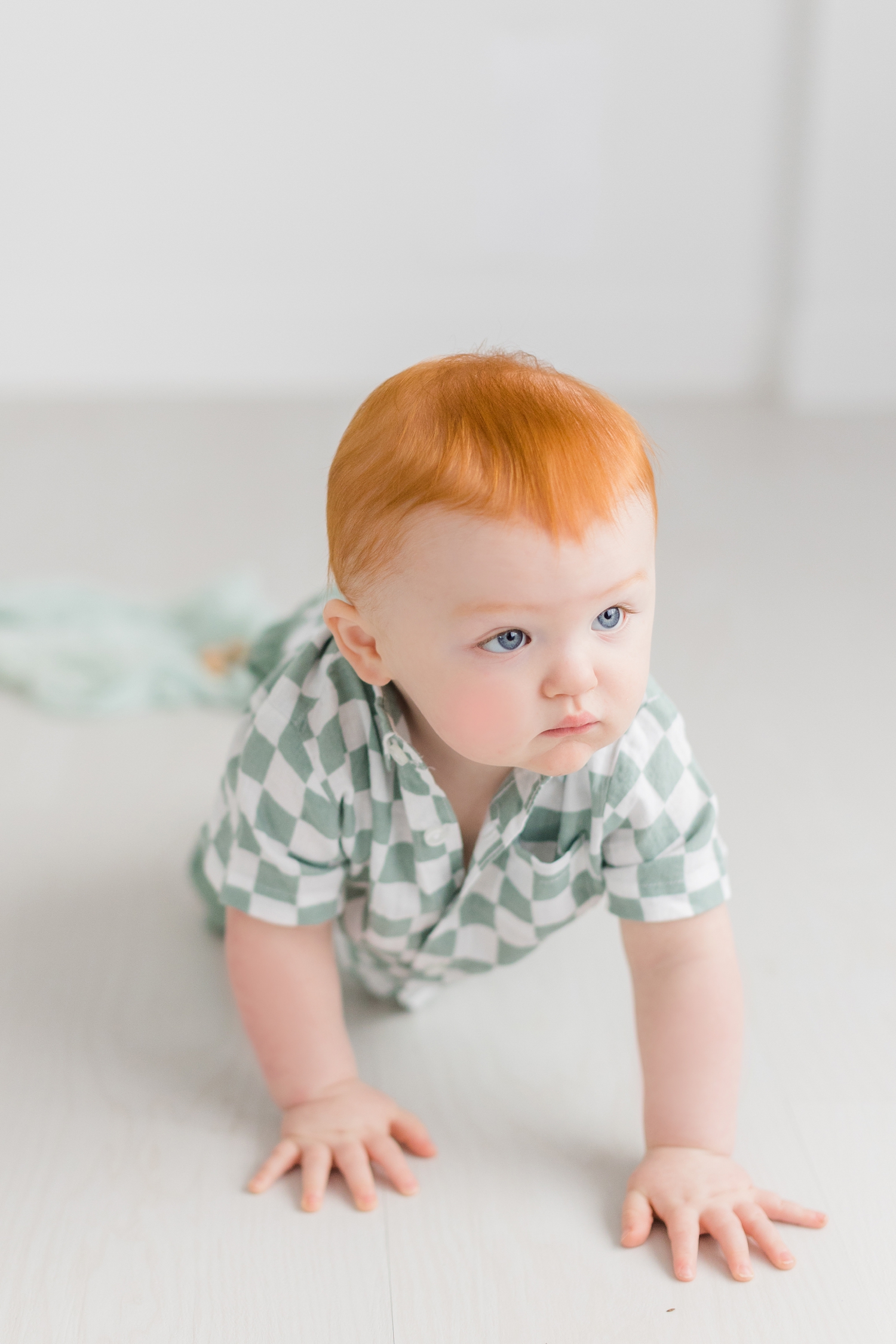 Baby Slater dressed in a mint green and white checkered button down, crawls across the floor of an all white photography studio | CB Studio