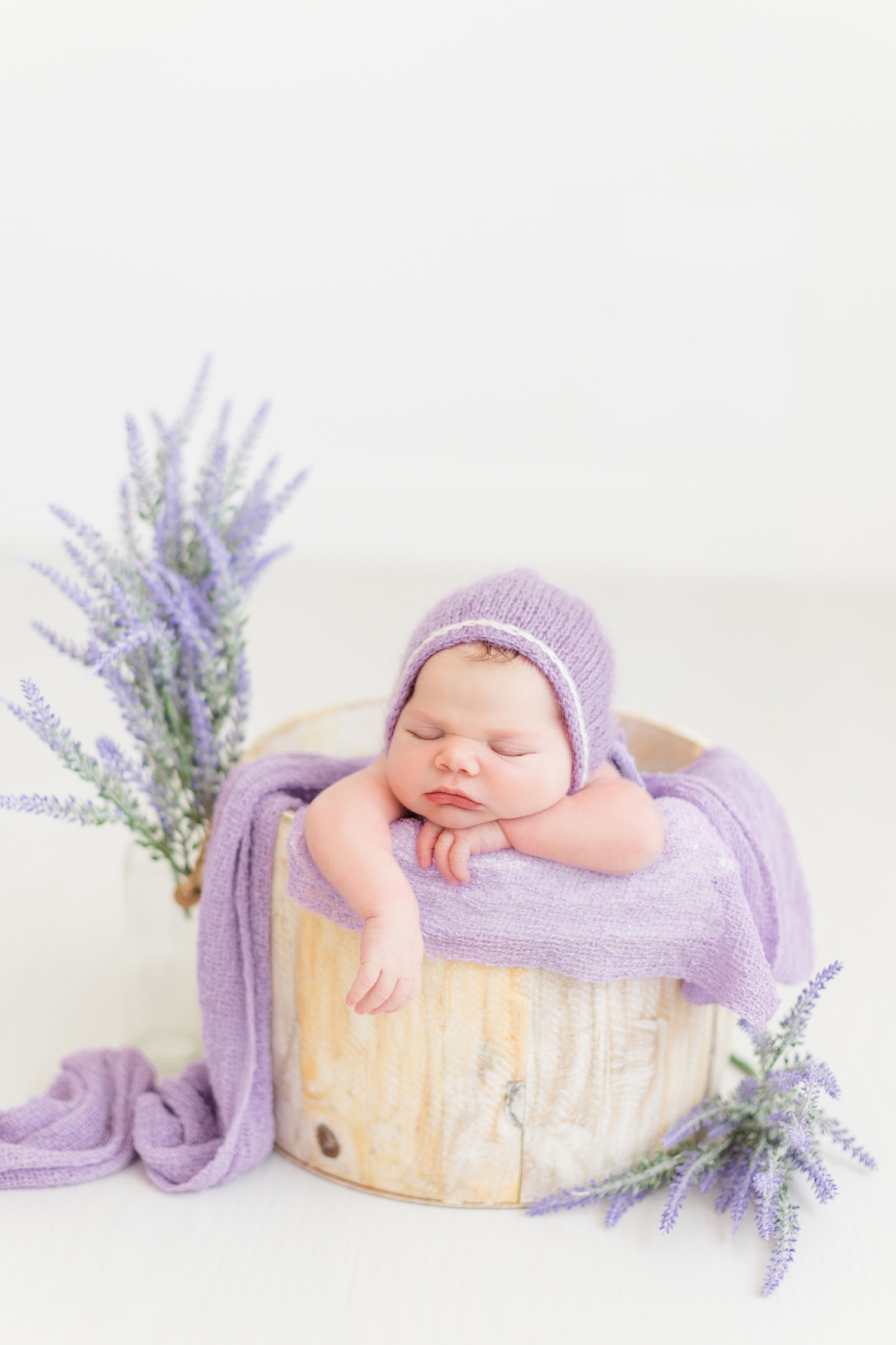 Baby Emersyn wearing a purple bonnet is snuggly nestled in a bucket surrounded by lavender | CB Studio