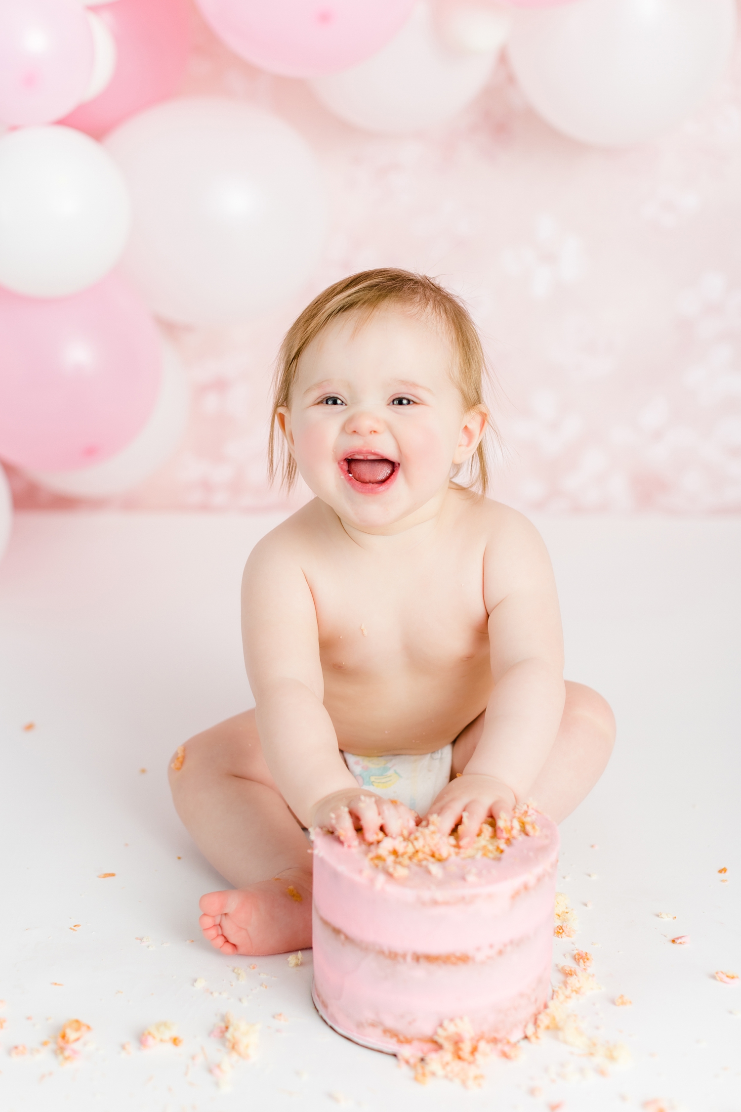 Baby Lauren smashes into her first birthday cake with a pink and white setup complete with balloon garland | CB Studio