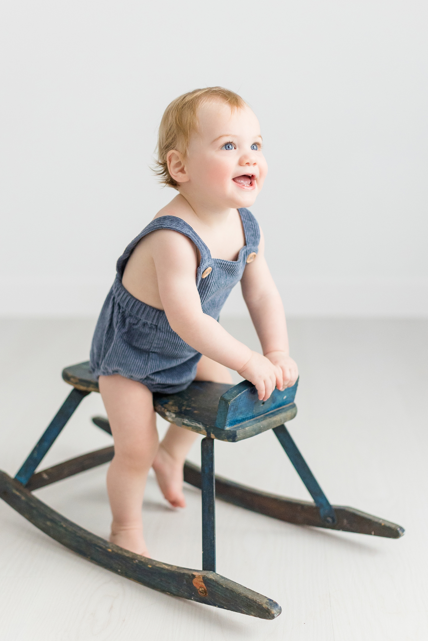 Baby Lewis wearing a blue corduroy romper plays on a blue rocking horse | CB Studio