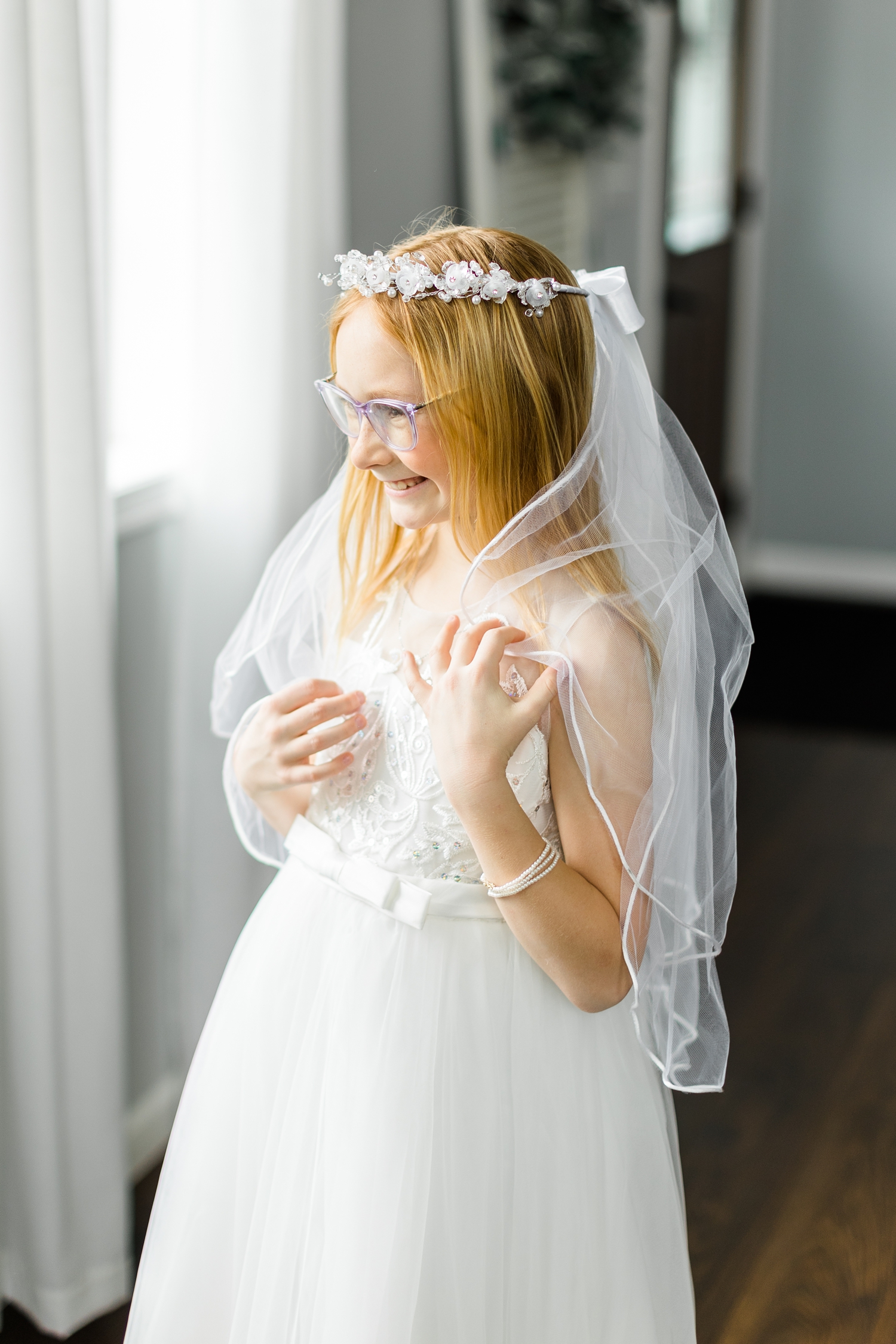 Liella First Communicant wraps her veil around her as she smiles while looking out the window | CB Studio