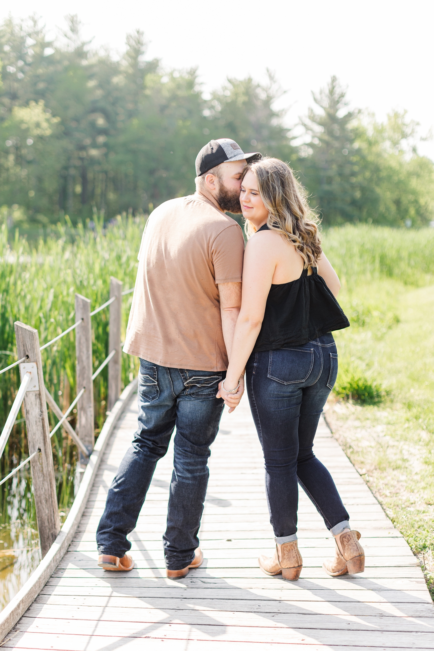 Matt whispers in to Megan's ear as they walk along a wooden deck path at Jester Park in Granger Iowa | CB Studio