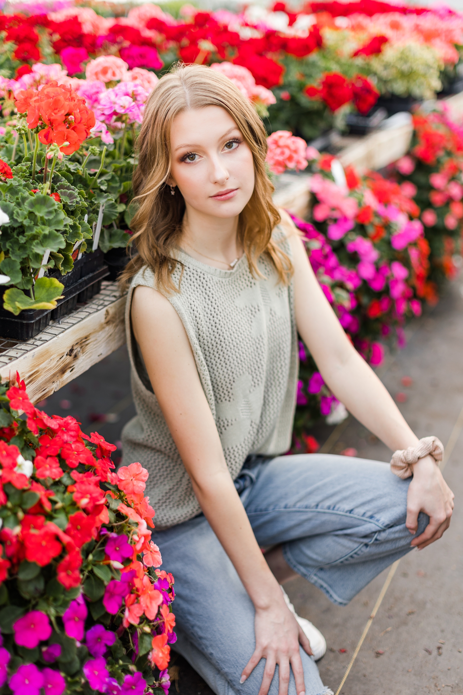 Senior spokesmodel Ryley sits surrounded by red, pink and magenta impatiens and geraniums in a greenhouse photoshoot | CB Studio