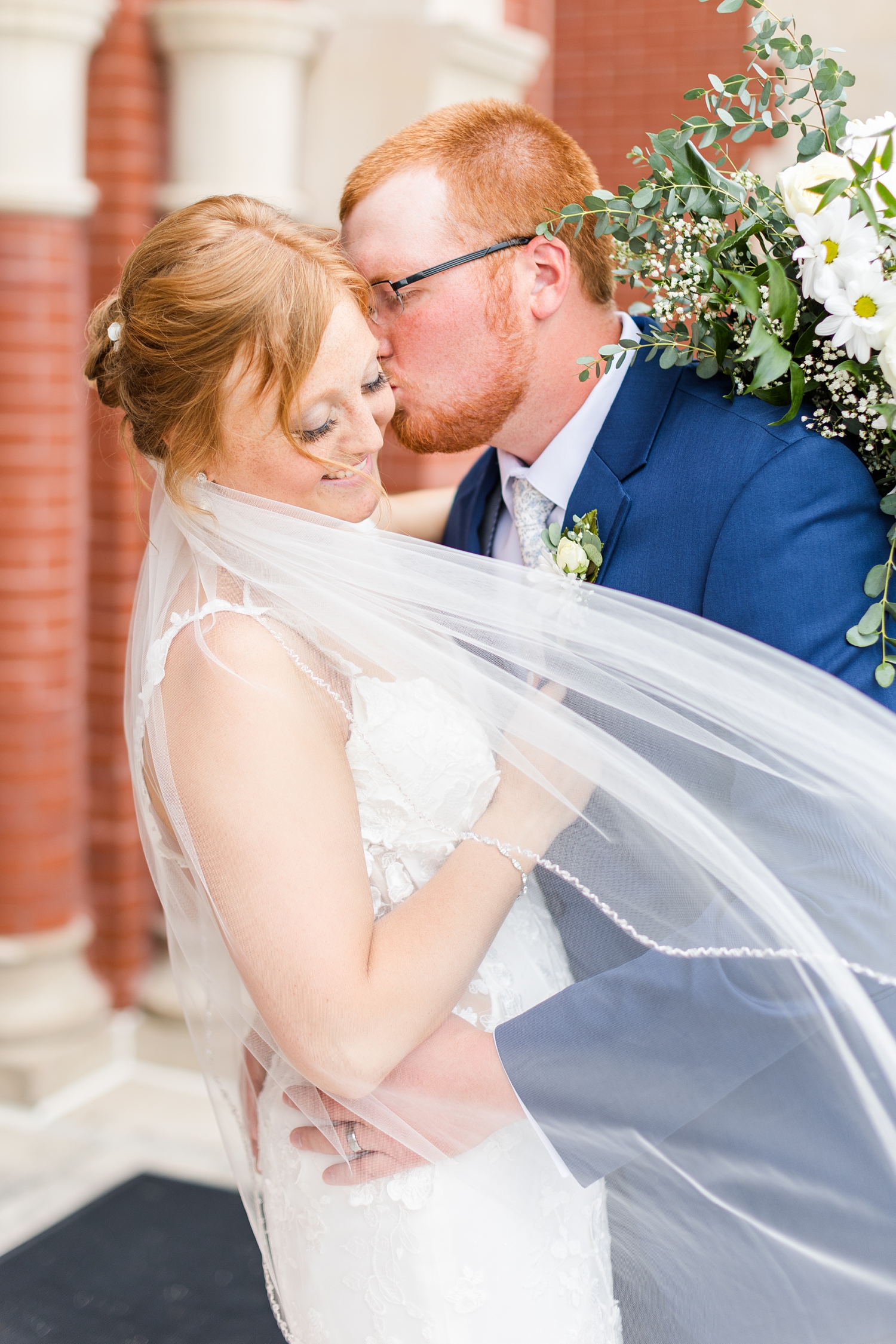 Matt kisses his new bride, Lauryn, on the cheek in front of the St. Joseph's Catholic Church in Mason City | CB Studio