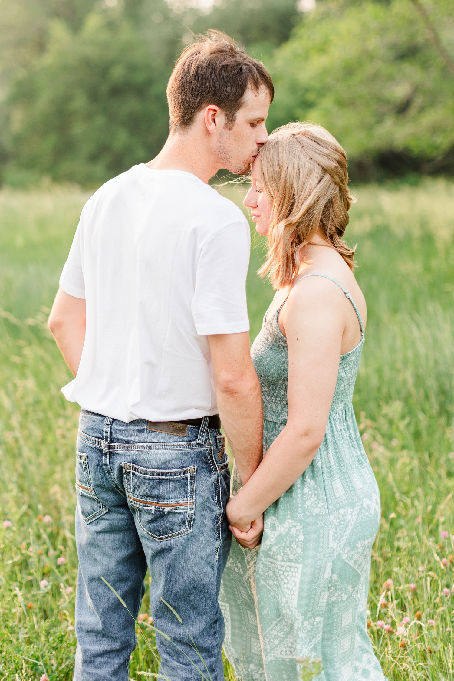 Zane gently kisses McKennan's head as they hold hands in a grassy field at sunset | CB Studio