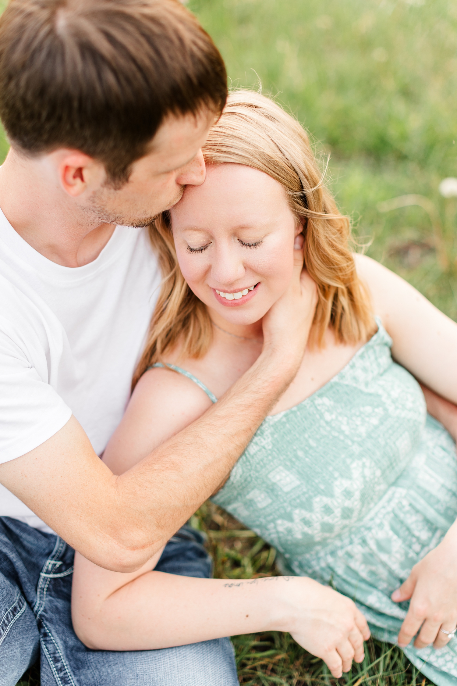 Zane gently kisses McKennan's head as she lays across his lap in a grassy field | CB Studio