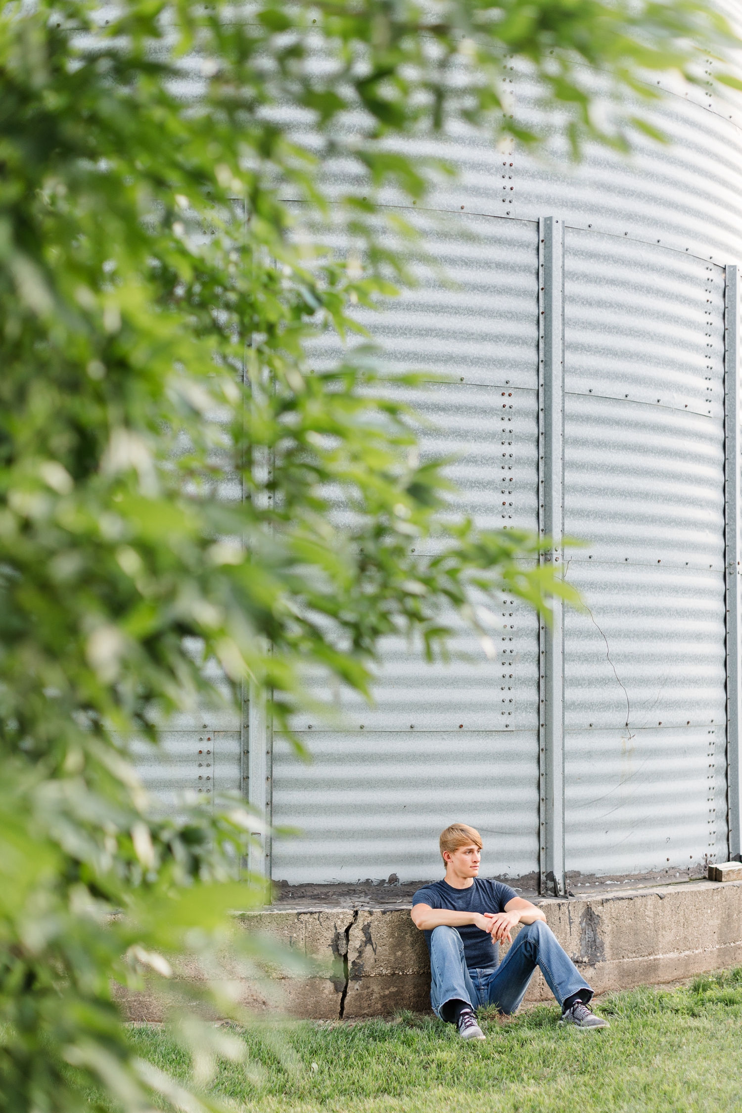Aidan sits against an grain bin on his family farm with leaves from a nearby branch framing him | CB Studio