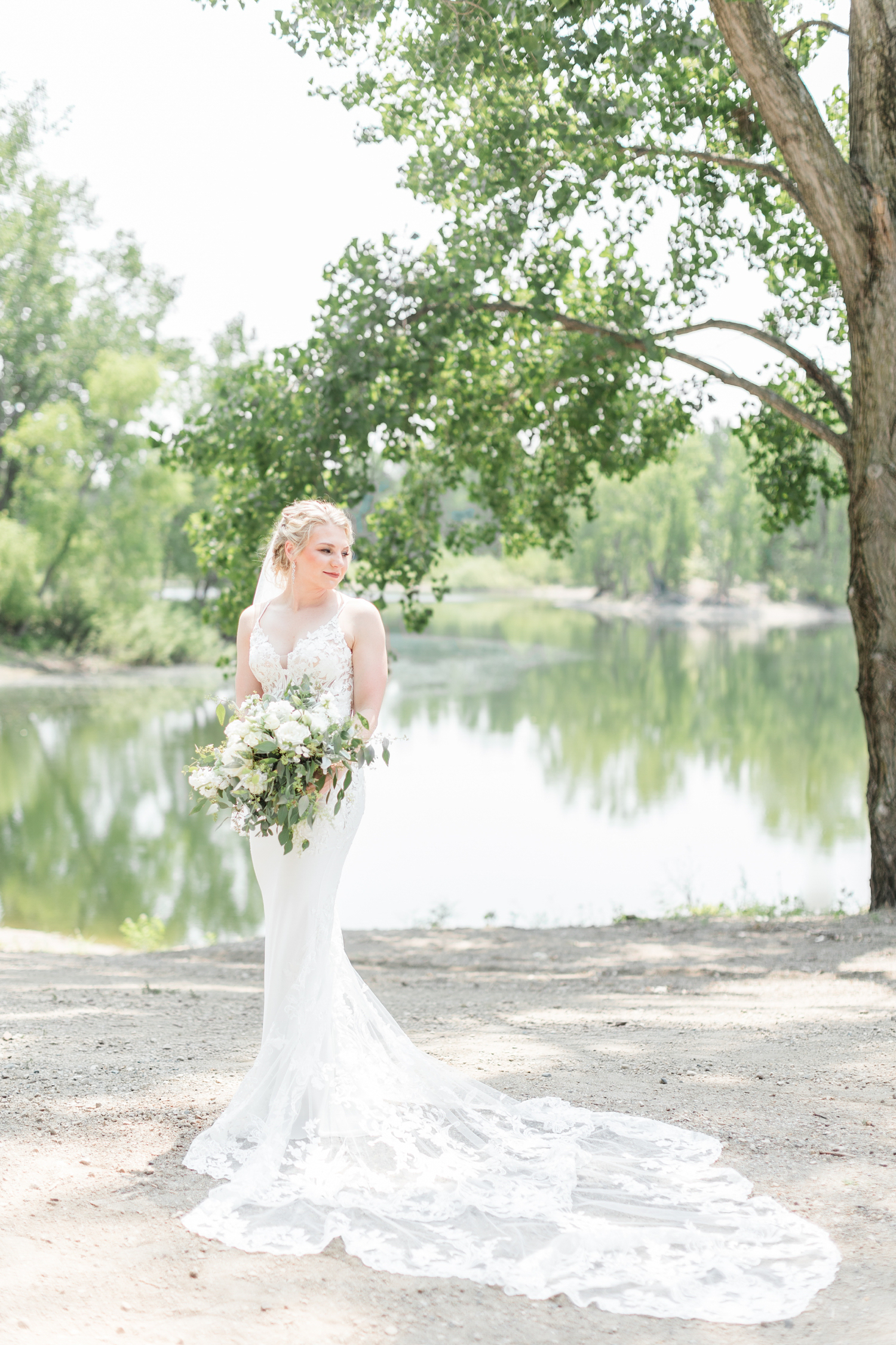 Alli looks down at her Enzoani wedding gown train in front of a scenic background at Wild Haven in Algona, IA | CB Studio