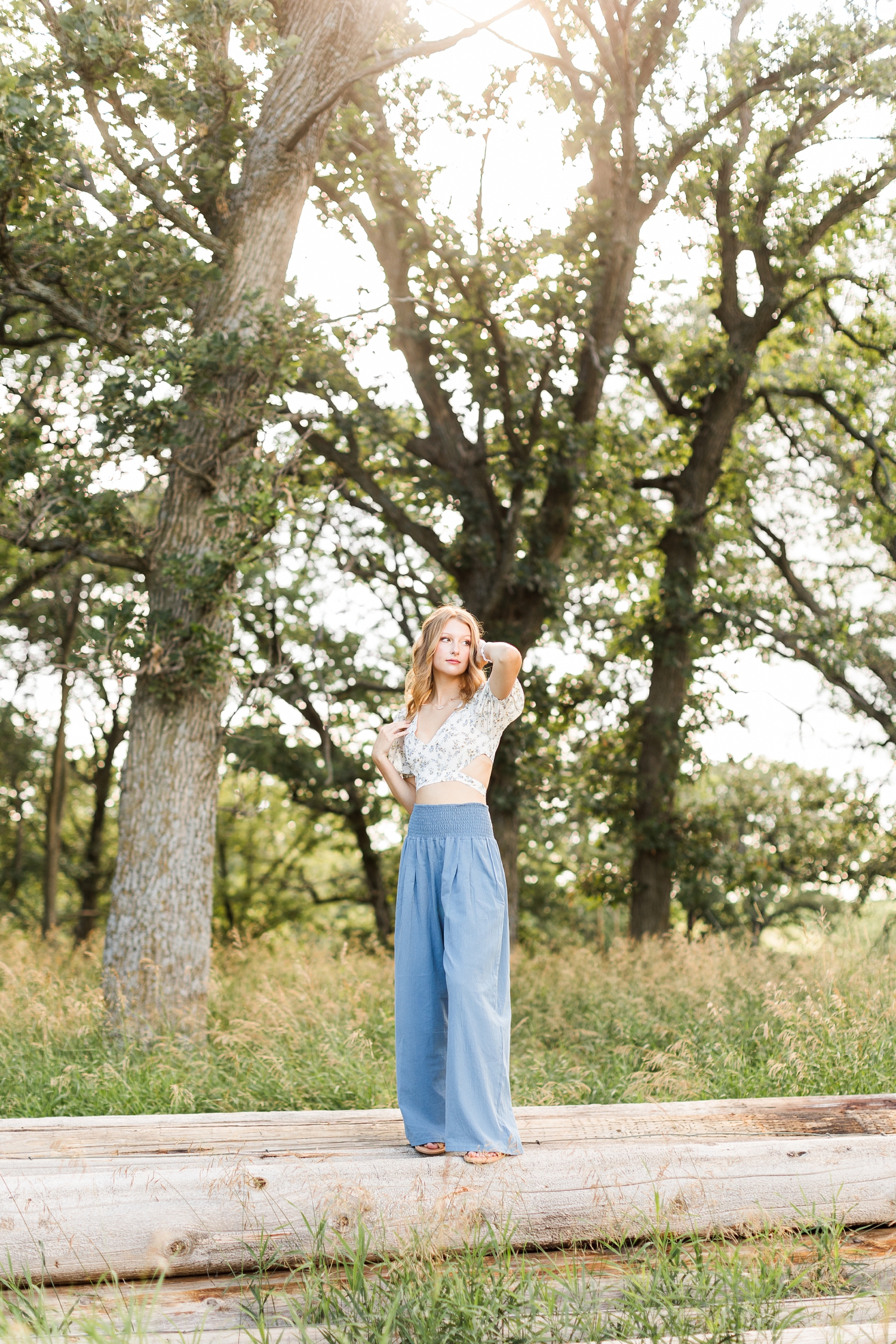 Ryley stands on a stack of cedar posts in a grassy pasture and looks off in the distance | CB Studio