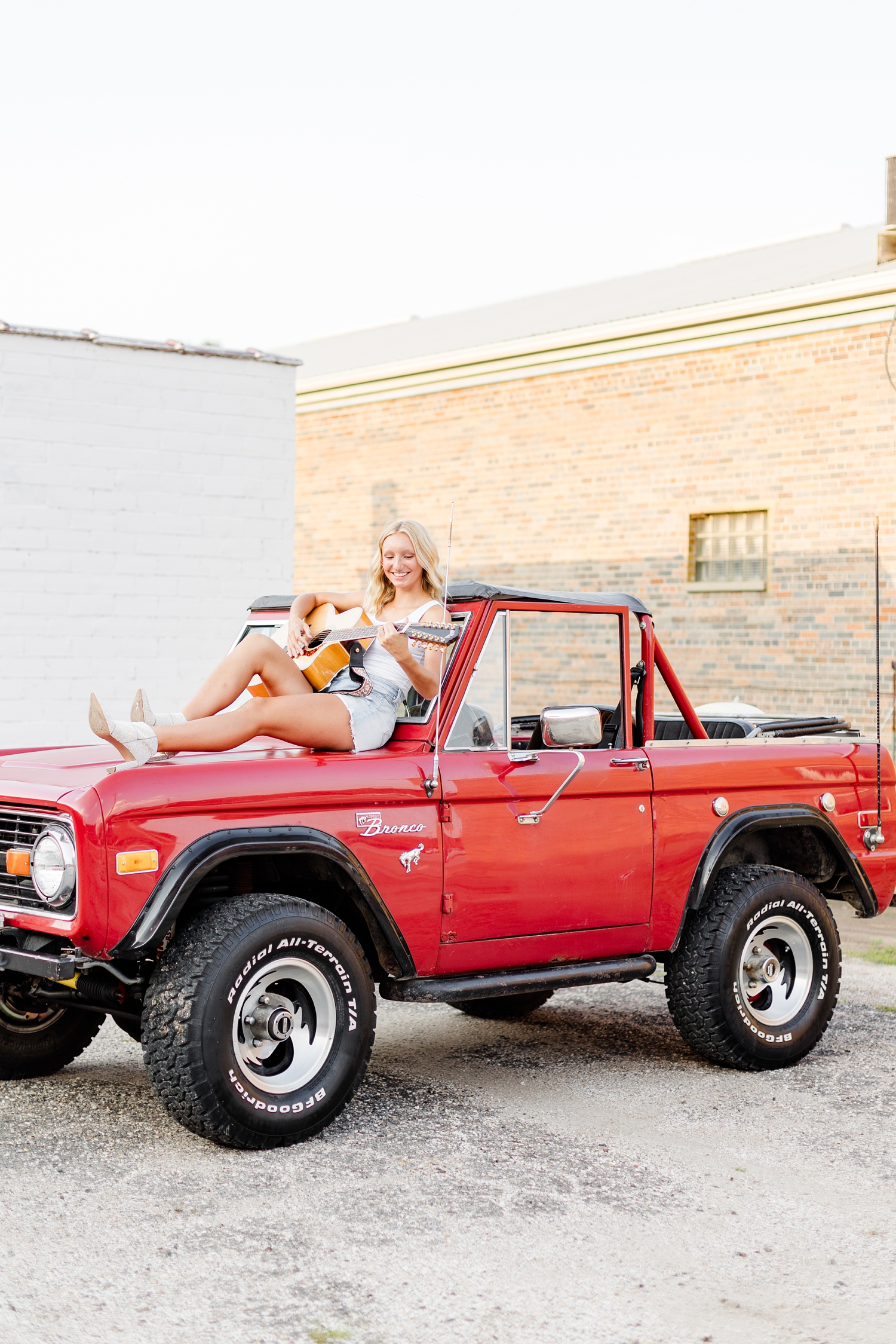 Avery plays her guitar while sitting on the hood of a 1974 red Bronco in downtown Algona, IA | CB Studio