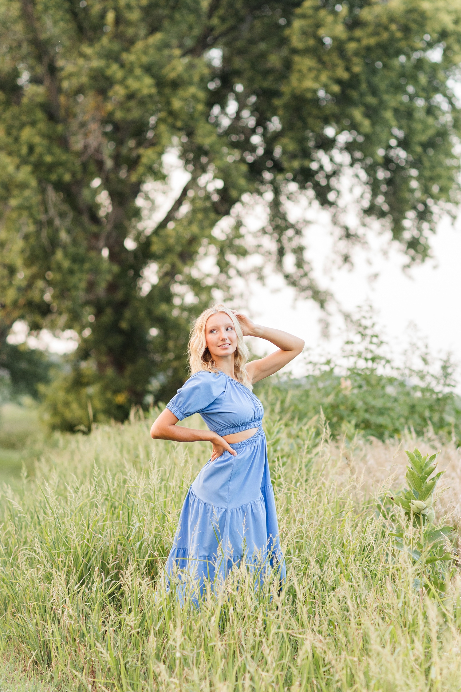Avery, wearing a long, flowy, blue dress, looks back over her shoulder in a grassy field | CB Studio