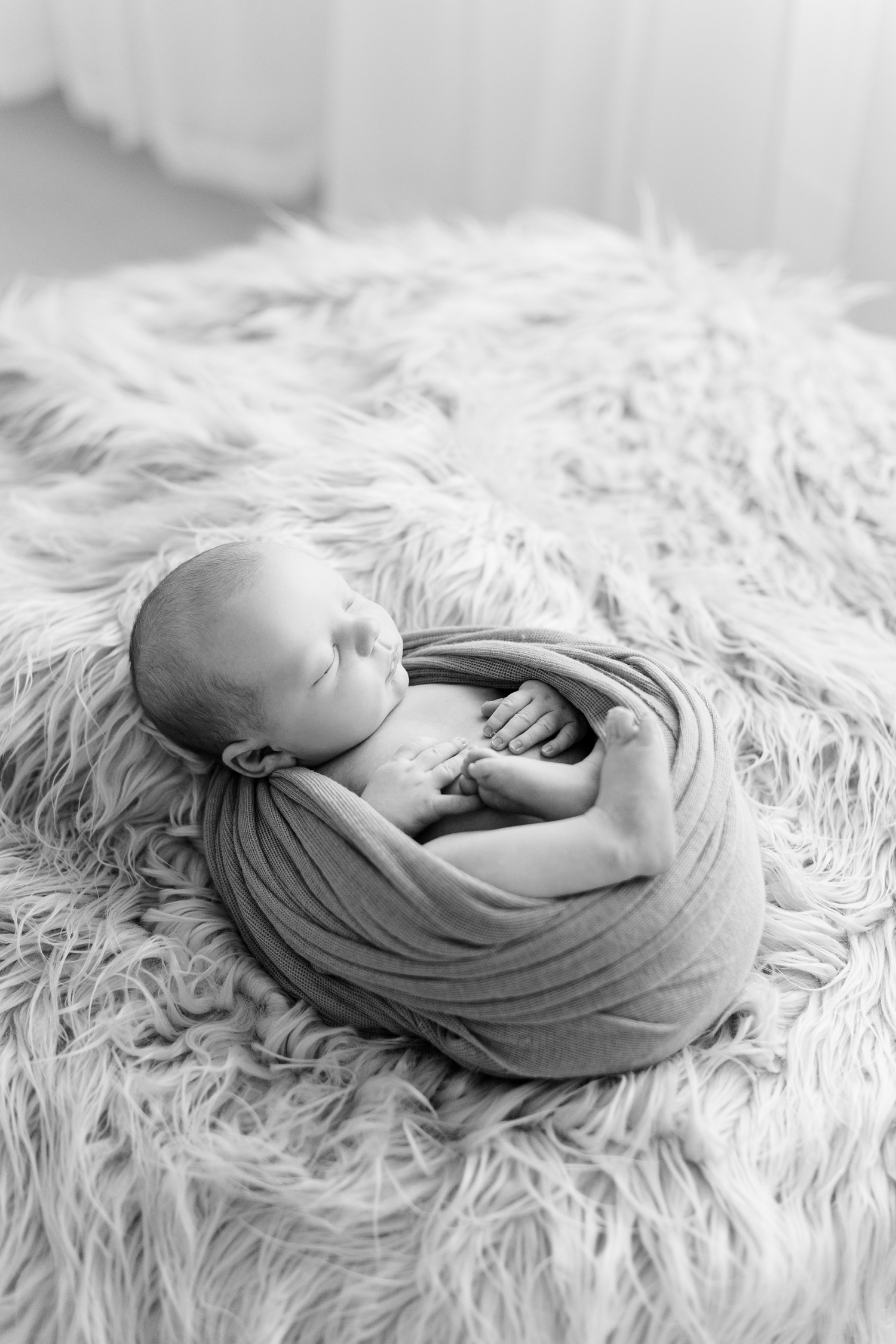 Baby Levi wrapped up in a swaddled laying on a flotaki rug with white curtains draped in the background | CB Studio
