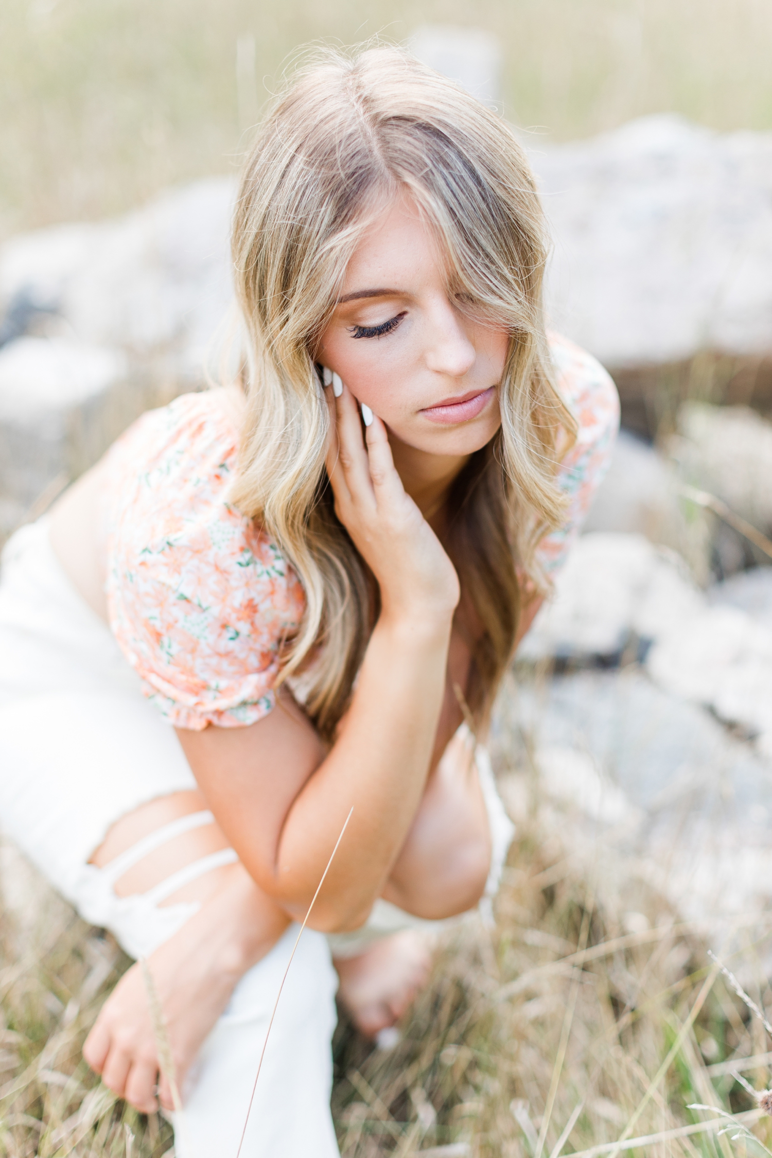 Eden looks down as she sits on large stones in the middle of a grassy field | CB Studio