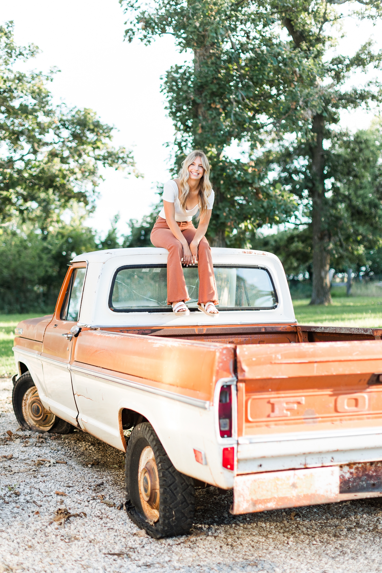 Eden, wearing burnt orange bell bottoms, sits on top of a 1970's two tone orange and white Ford truck | CB Studio