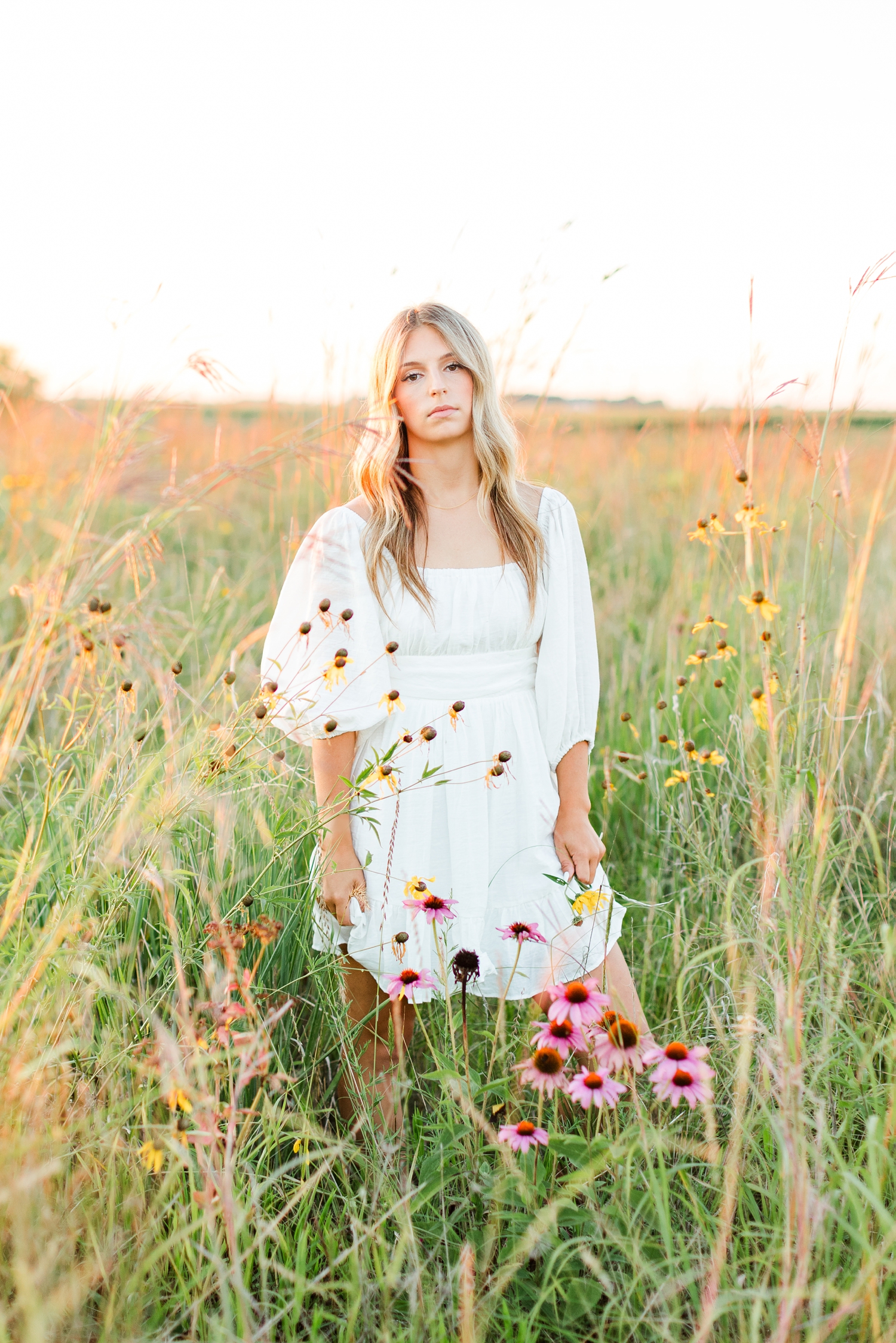 Eden stands in a wildflower field at golden hour wearing a white dress | CB Studio