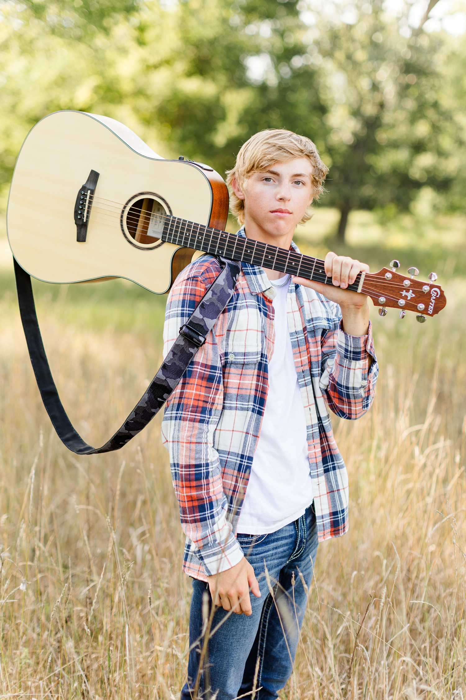 Justin stands in the middle of a grassy field with his guitar on his shoulder | CB Studio