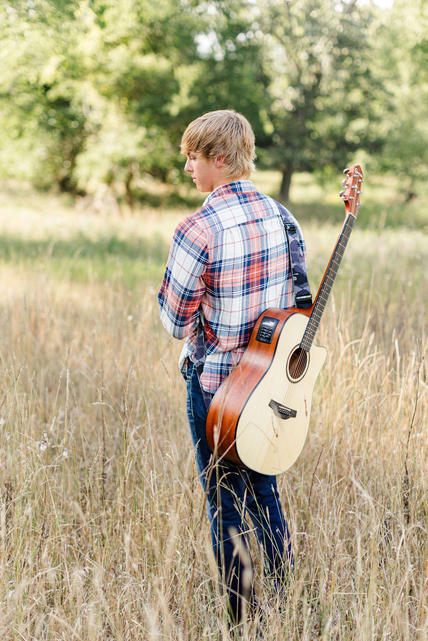 Justin stands in the middle of a grassy field with his guitar strapped to his back | CB Studio