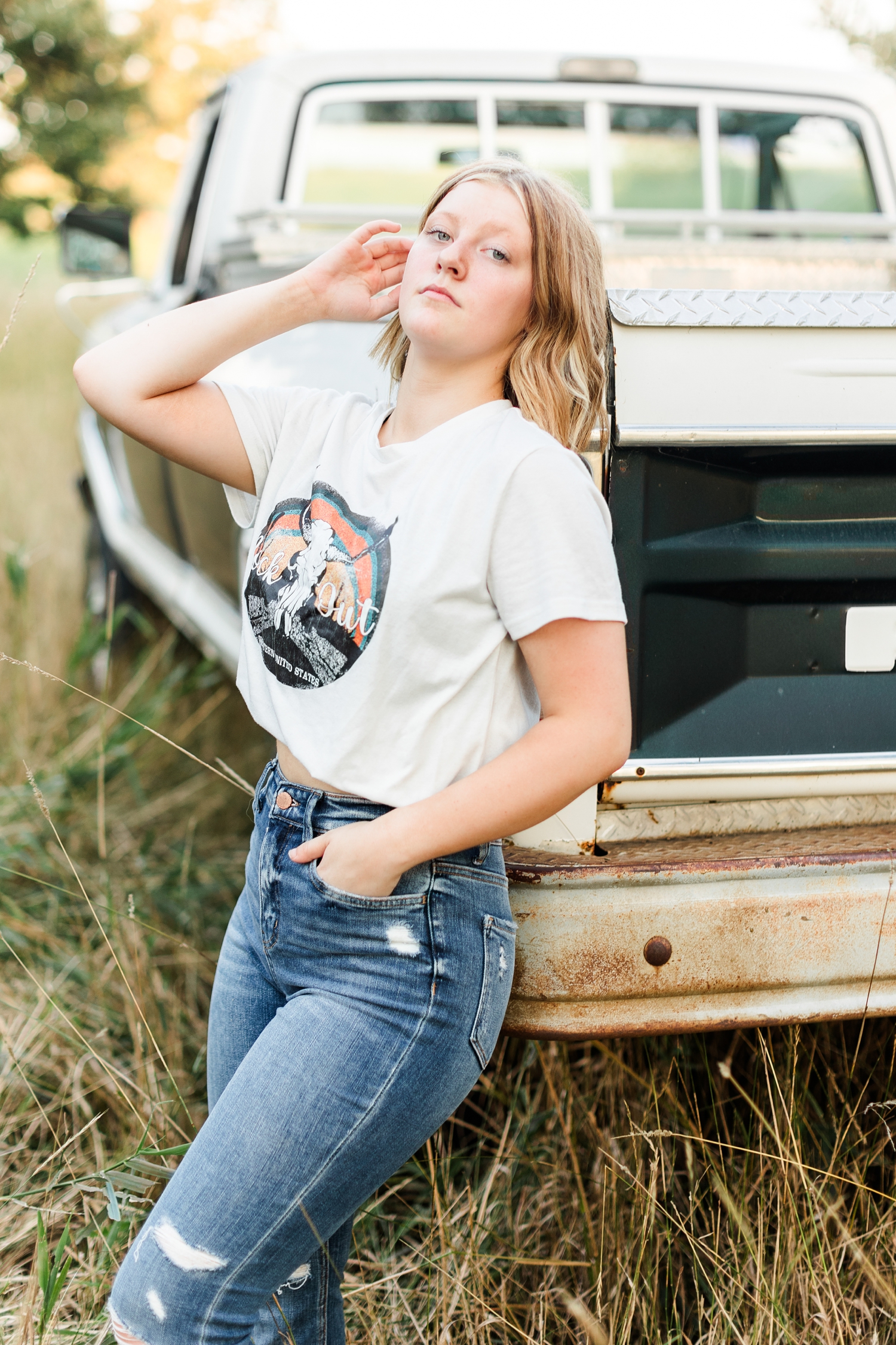 Kenzie leans on the back of a 70's Ford Highboy truck in the middle of a grassy field | CB Studio