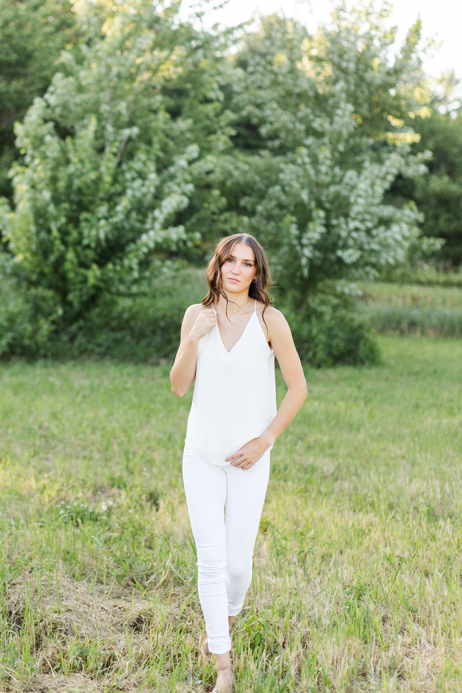 Mallory walks in a grassy field wearing white jeans and a white tank top | CB Studio