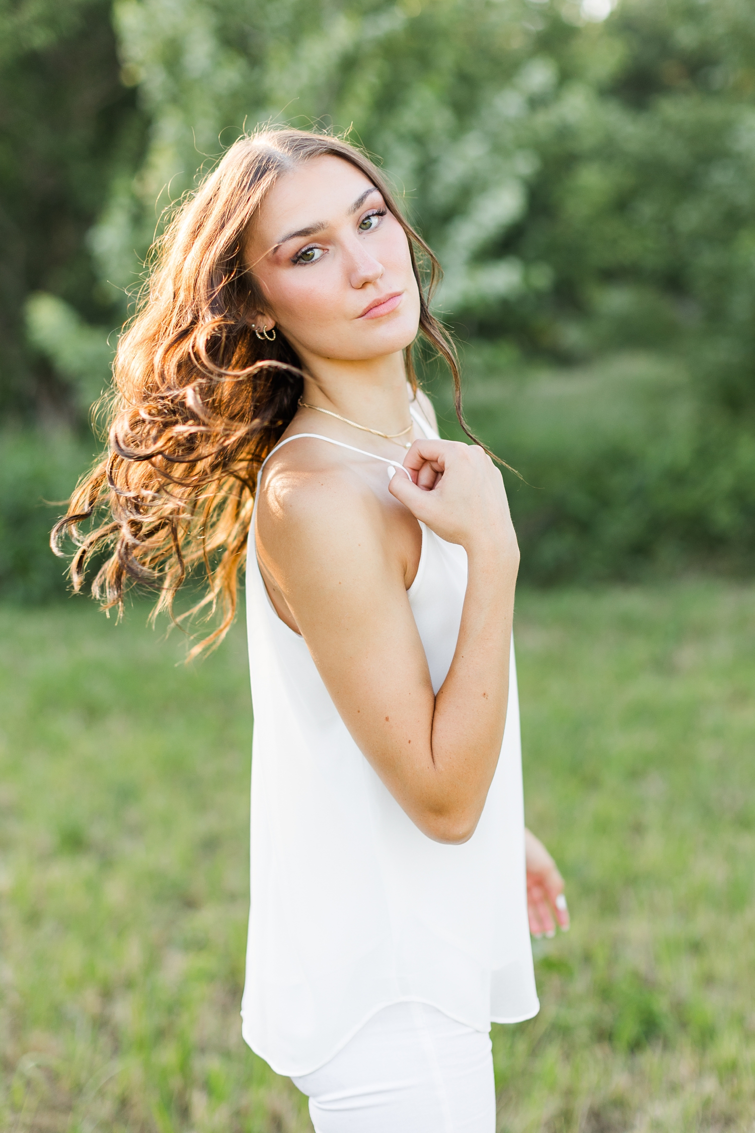 Mallory turns over her shoulder with her hair blowing in the wind wearing white jeans and a white tank top | CB Studio