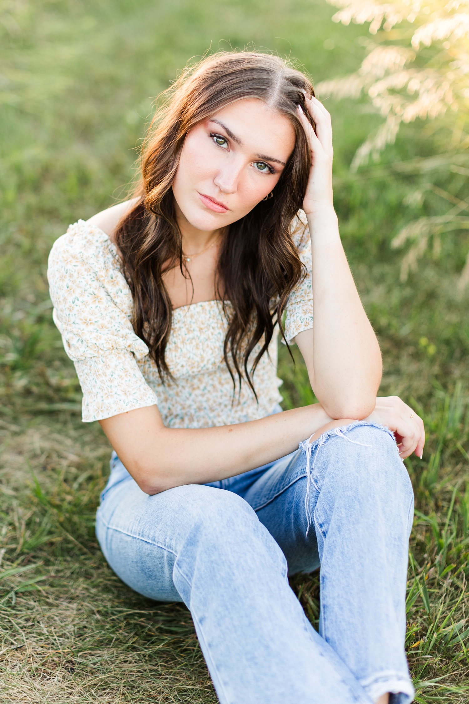 Mallory sits in a grassy field at Water's Edge Nature Center wearing jeans and a smocked floral top | CB Studio