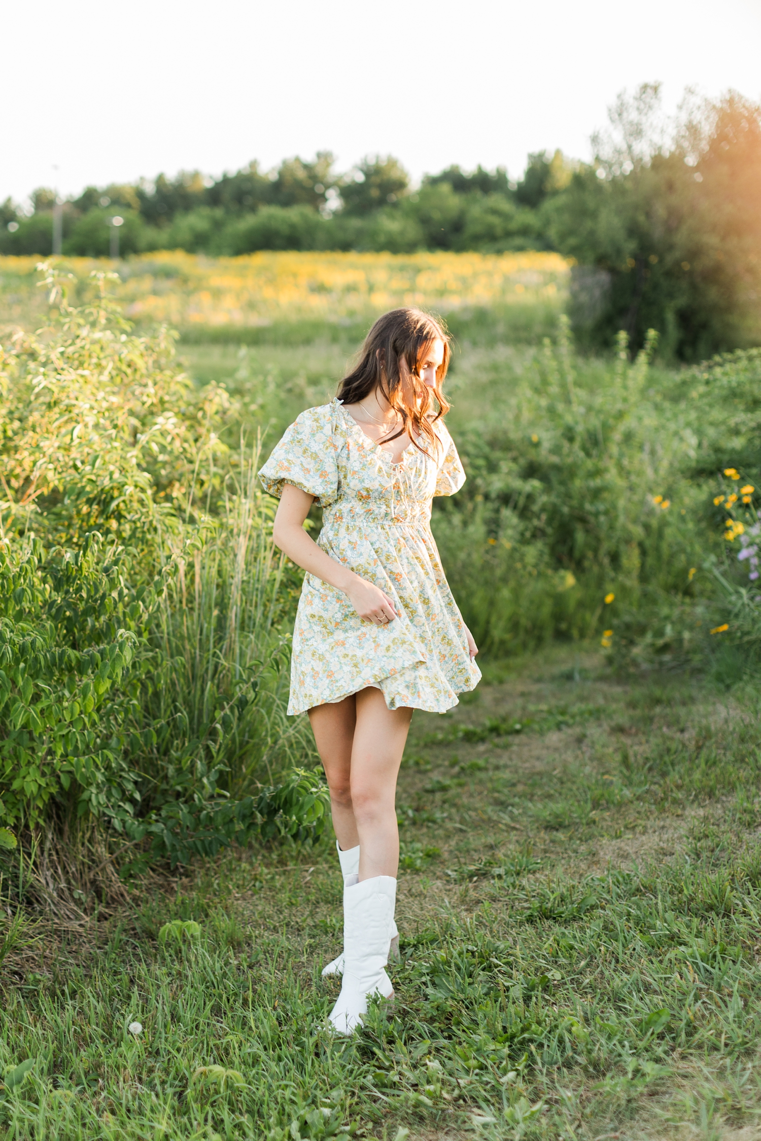 Mallory dances in a field of yellow wildflowers wearing a green and yellow floral dress and white cowgirl boots | CB Studio