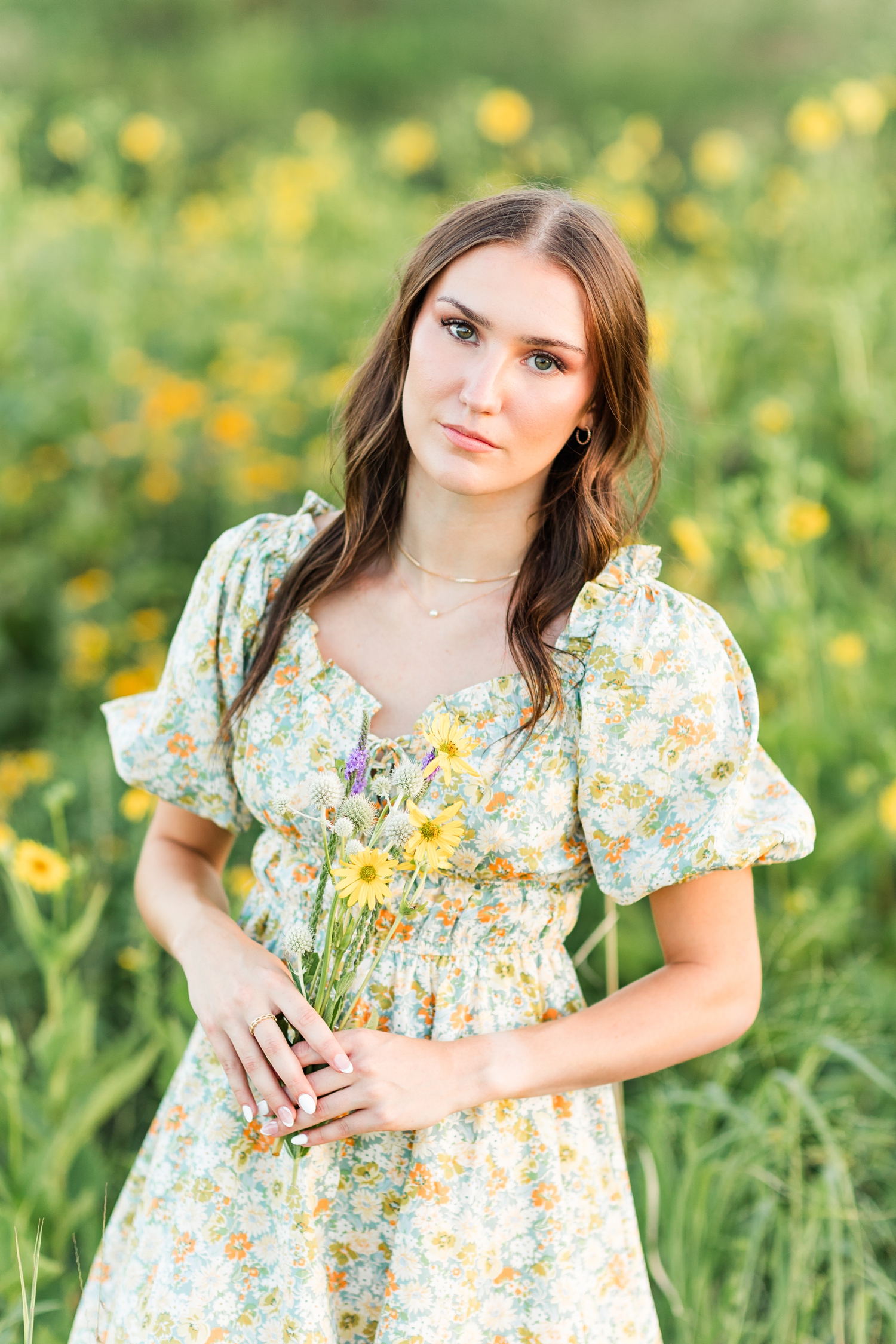 Mallory holds a wildflower bouquet in a field of yellow wildflowers wearing a green and yellow floral dress | CB Studio