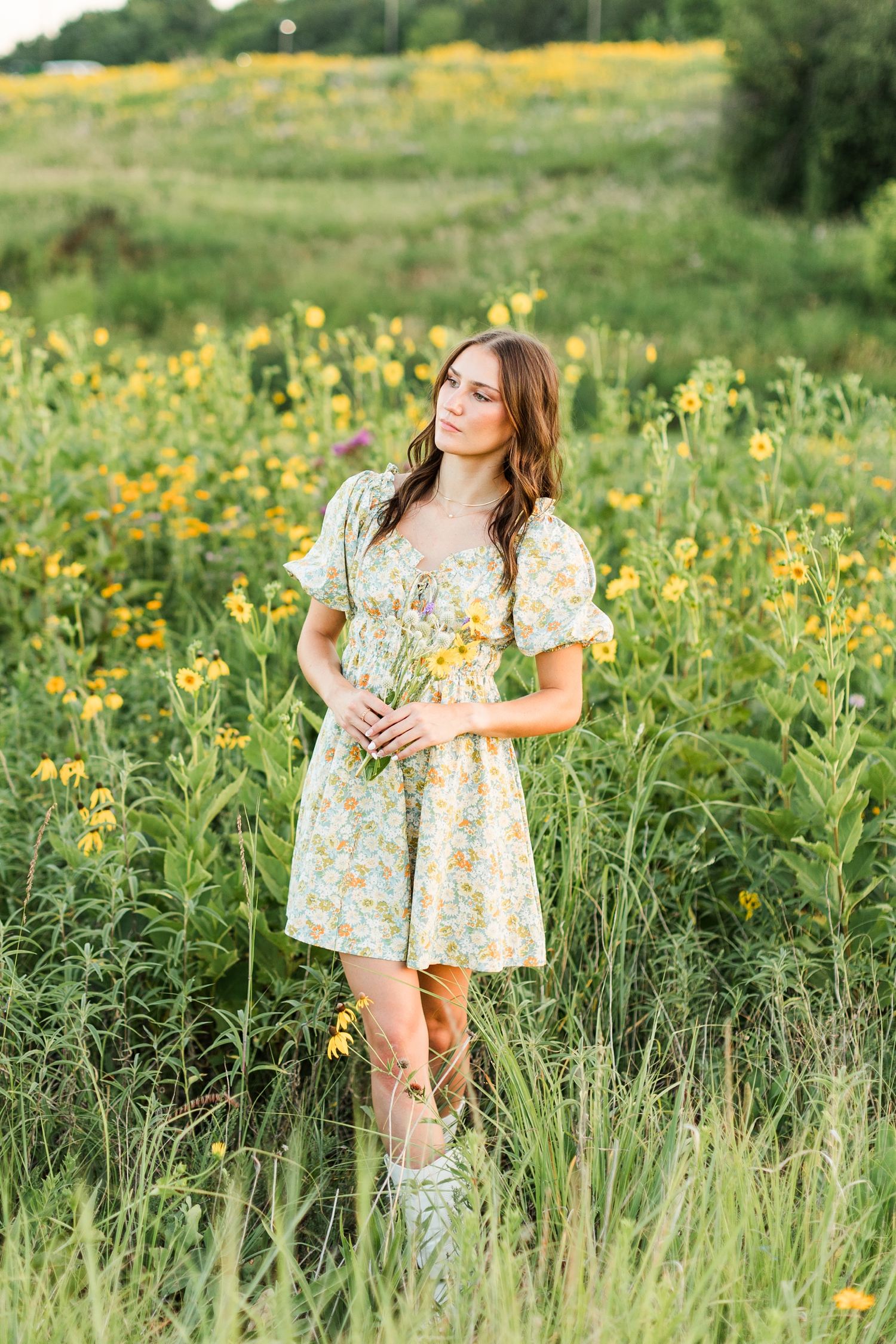 Mallory holds a wildflower bouquet in a field of yellow wildflowers wearing a green and yellow floral dress | CB Studio