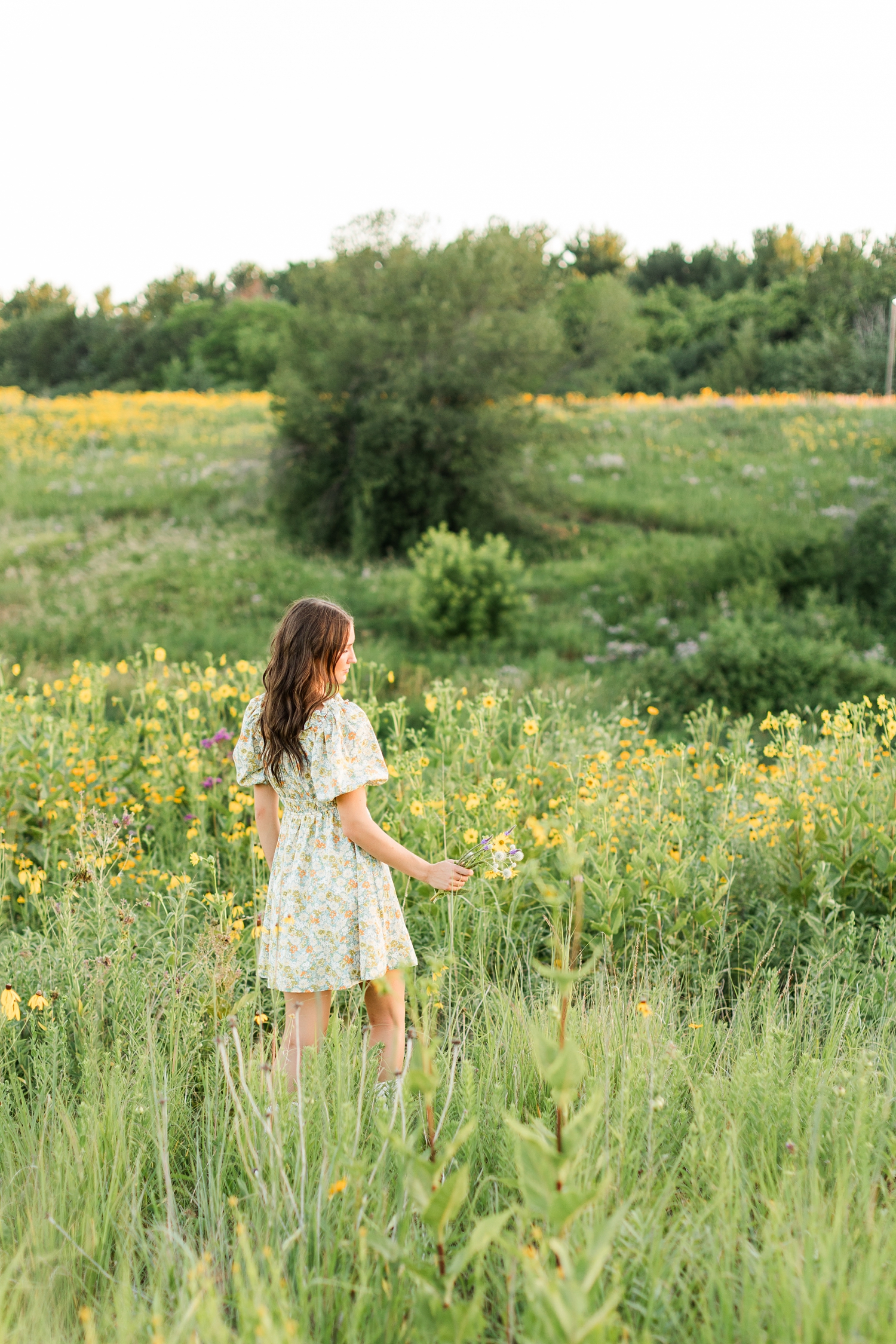 Mallory walks through a field of wildflowers wearing a green and yellow floral dress | CB Studio