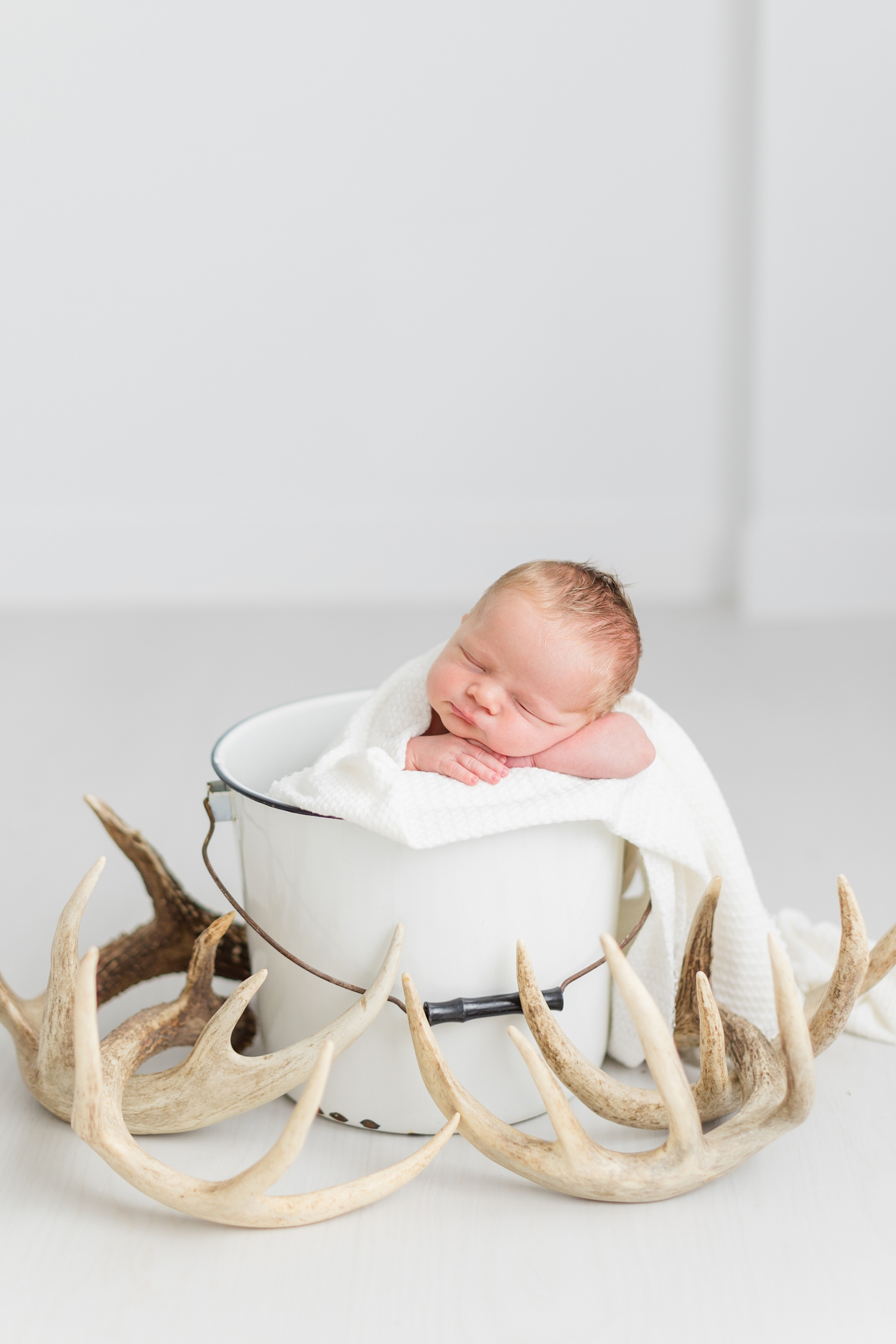Baby Wyatt sleeps peacefully in a white bucket surrounded by deer antlers | CB Studio