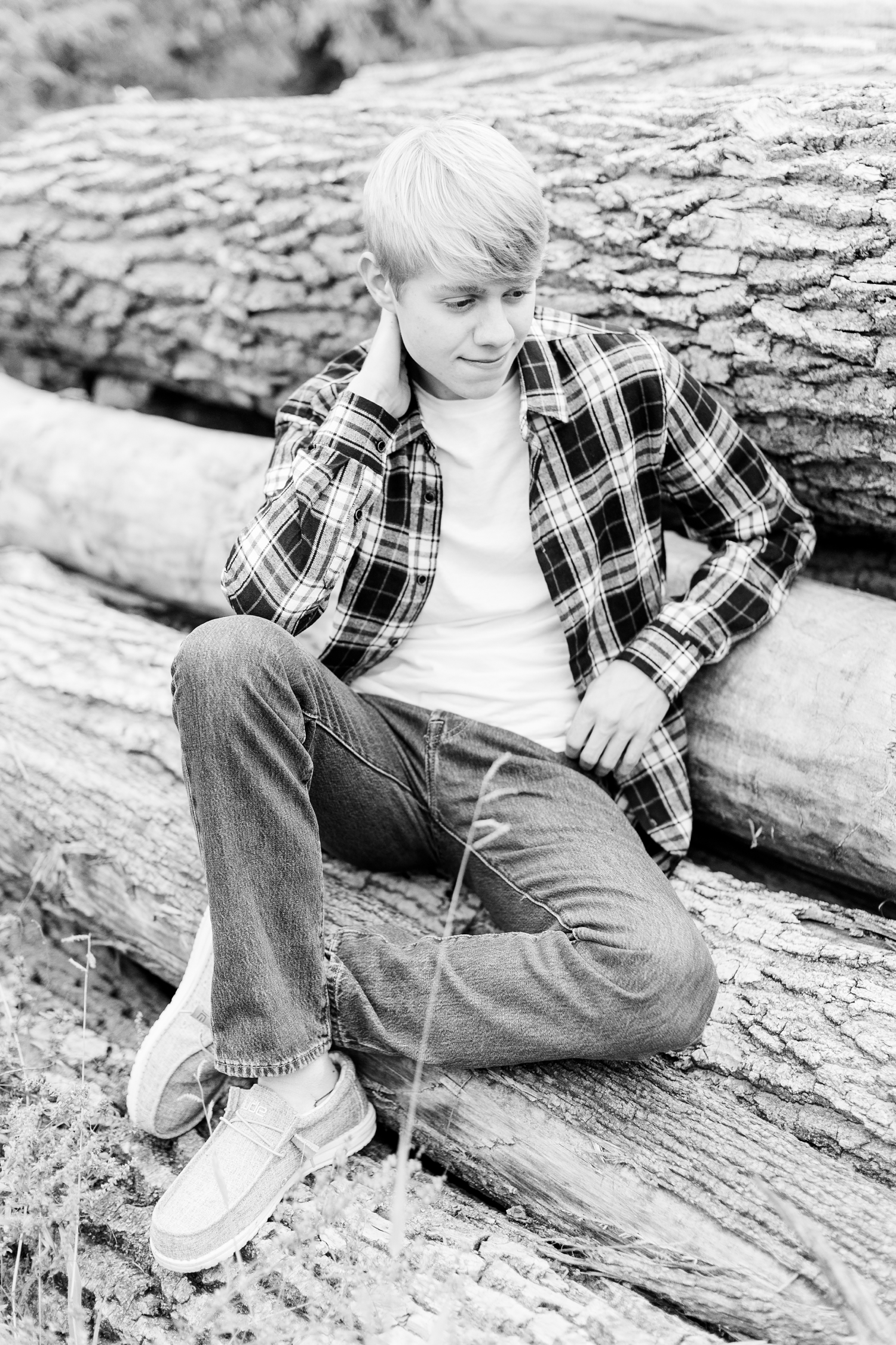 CJ sits on a pile of logs while looking down his grandpa's farm in northern Iowa | CB Studio