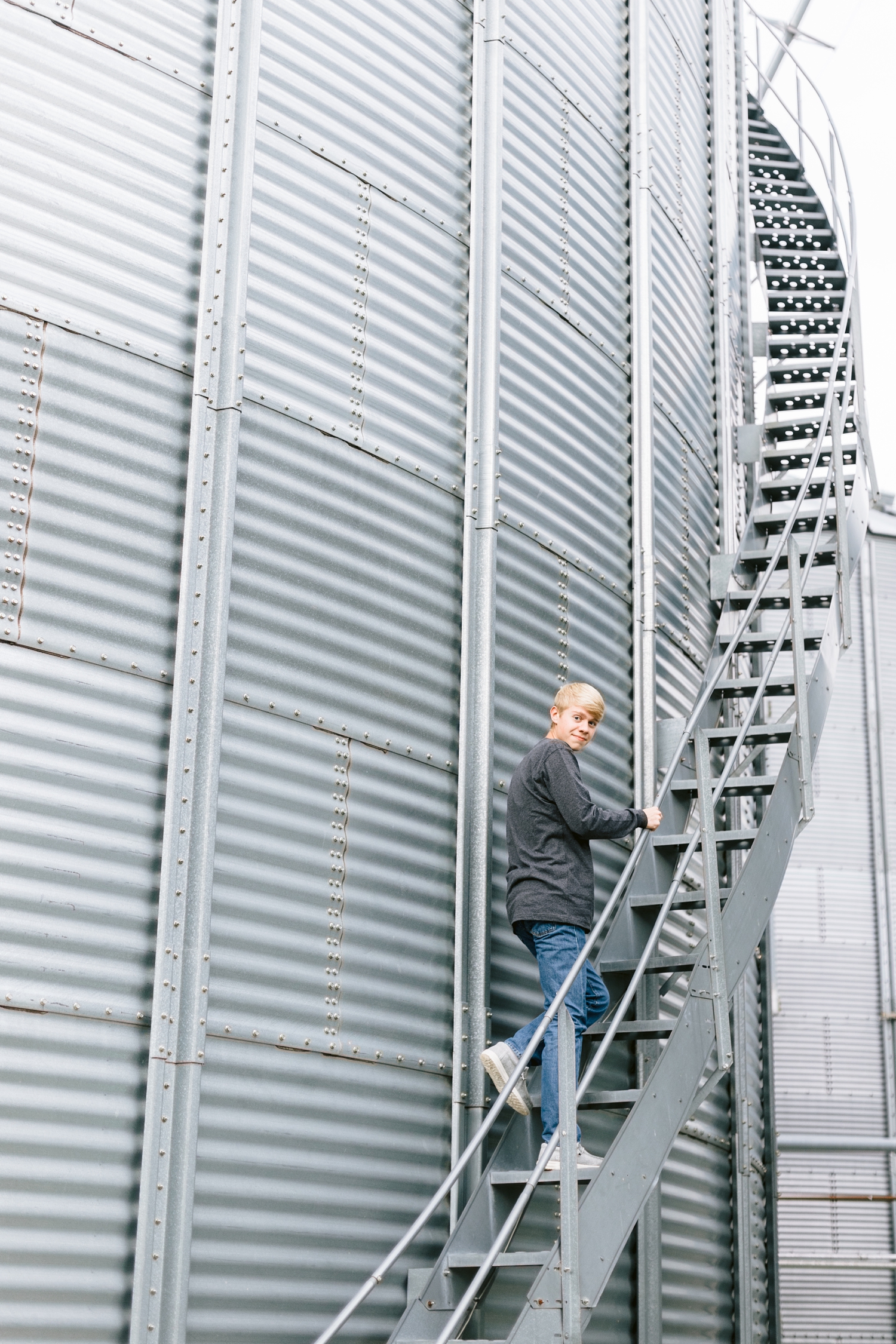 CJ smiles back as he walks up the long winding staircase of a grain bin at his grandpa's farm in northern Iowa | CB Studio