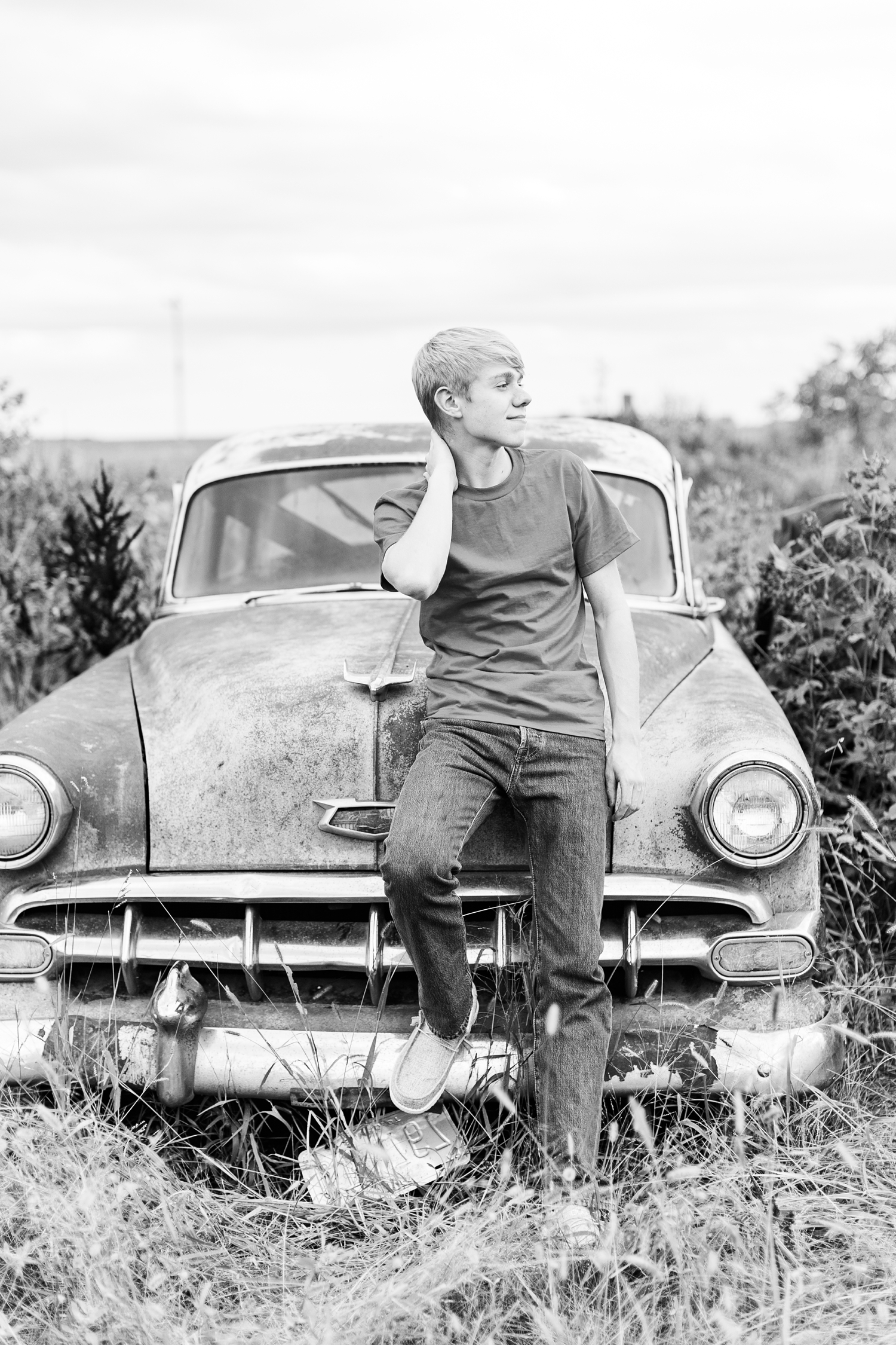 CJ sits on the hood of his grandpa's vintage Chevy that has been sitting in a pasture for several years | CB Studio