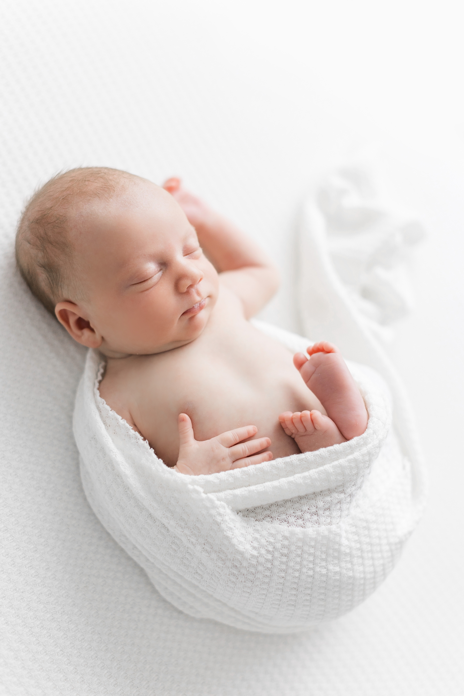 Baby Elizabeth half wrapped in white sleeping on an all white background | CB Studio