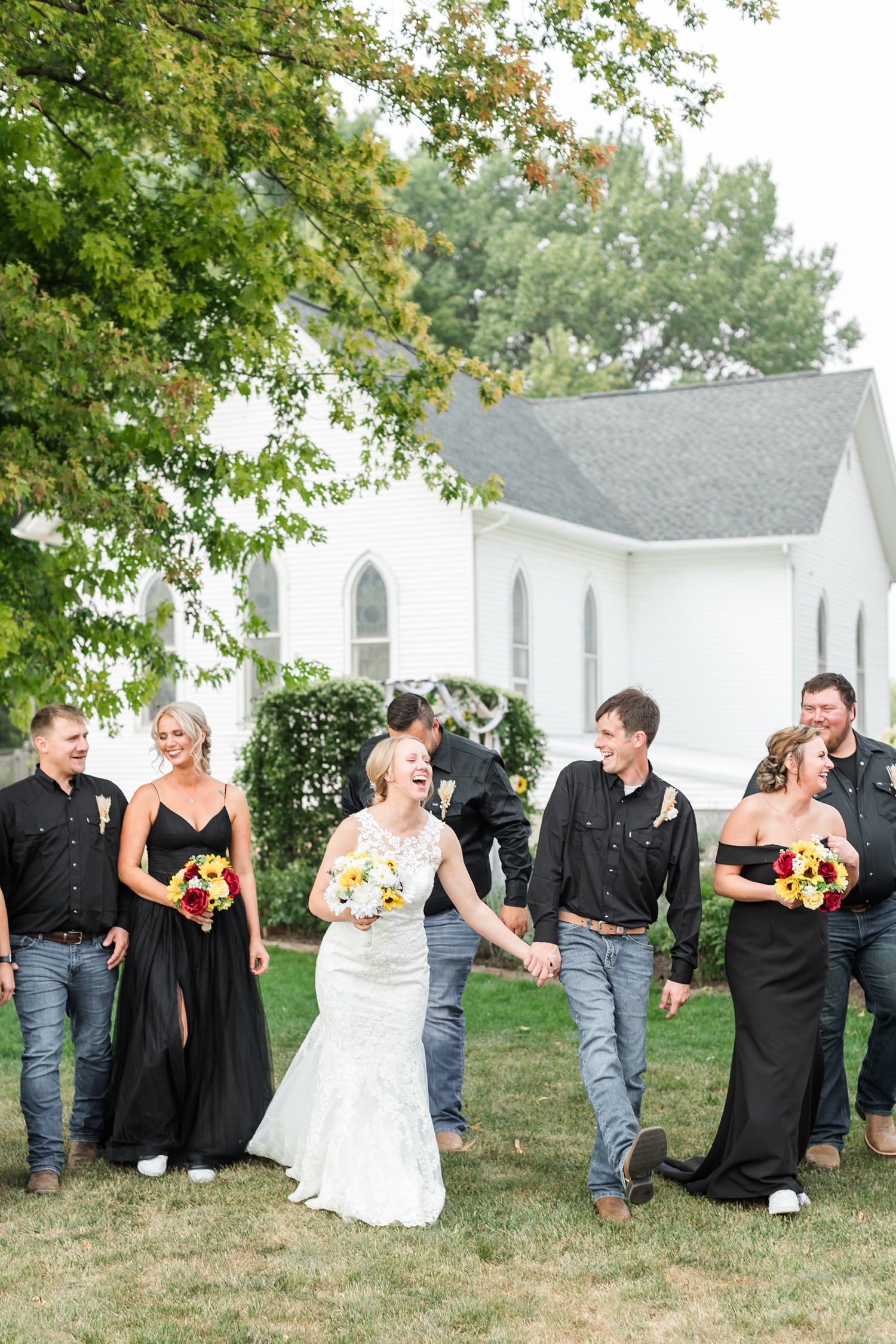 Mckennan and Zane laugh as they walk with their wedding party her in the garden space at the Humboldt County Museum with the Hardy church in the background | CB Studio