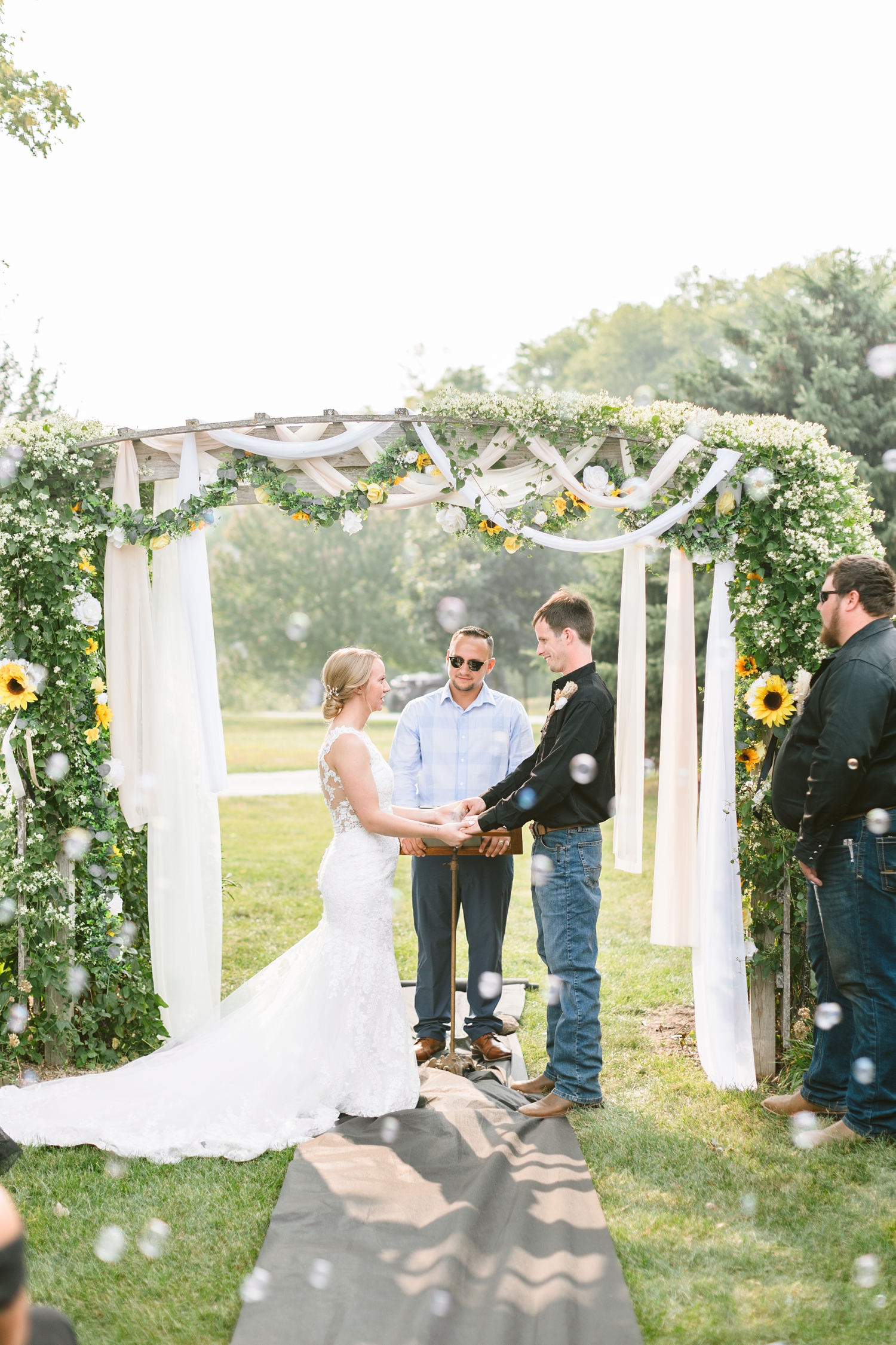 Mckennan and Zane say their wedding vows surrounded by bubbles beneath a floral gazebo arch with draping fabrics in the garden space at the Humboldt County Museum | CB Studio
